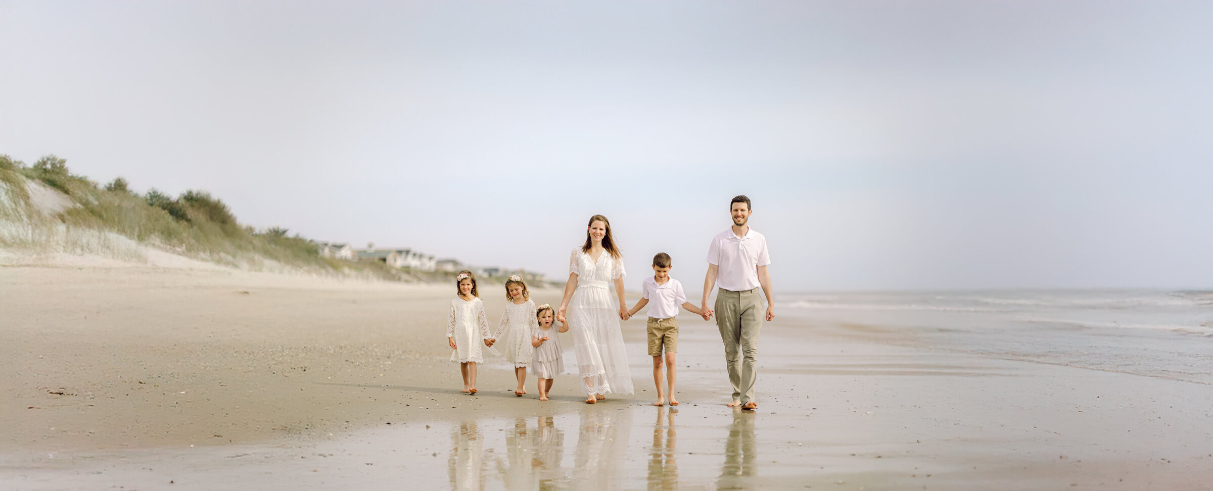 A photo of the family holding hands walking on the beach of the Outer Banks