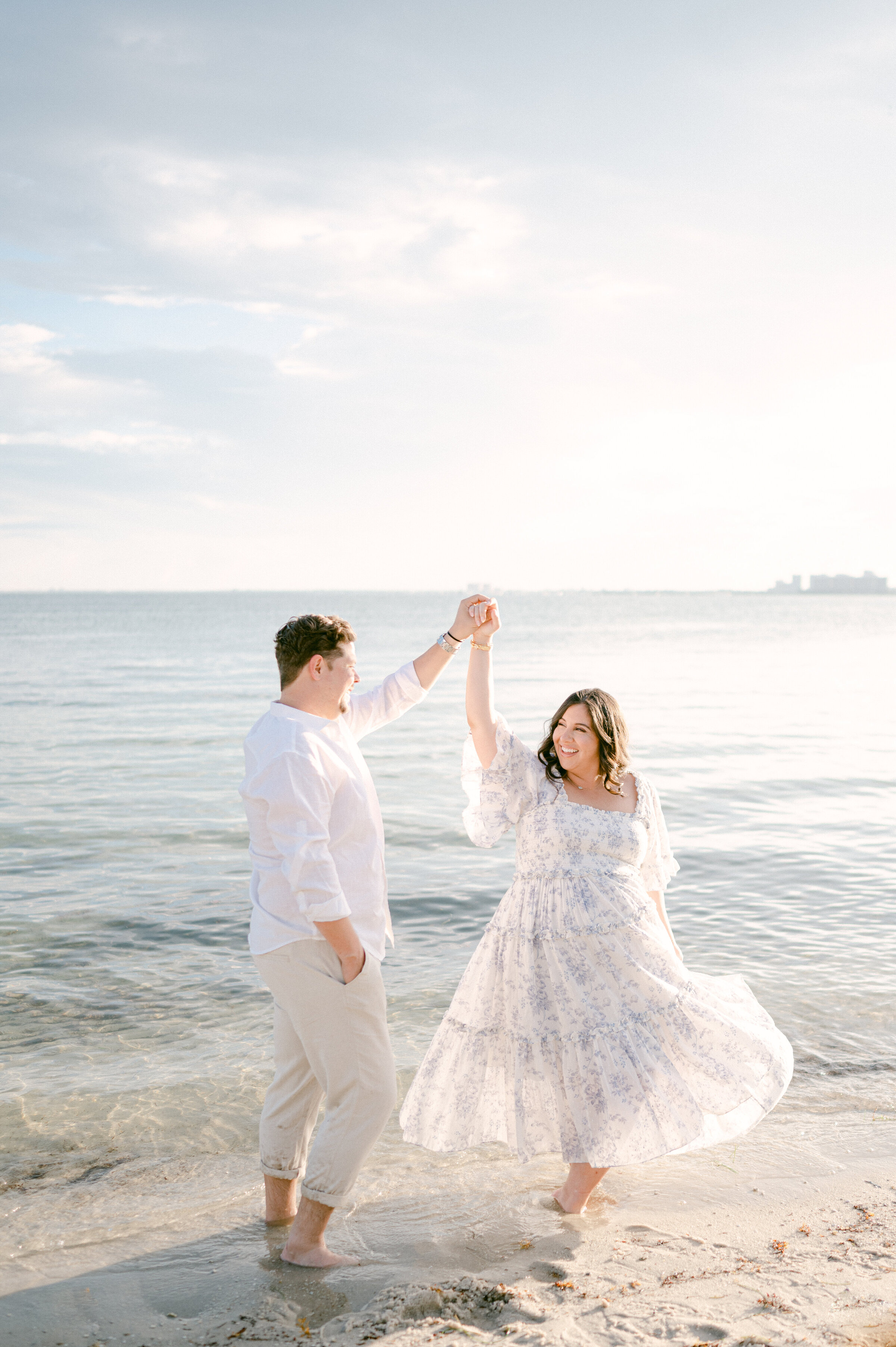 Pregnant couple dancing on the beach with sunlight going through the dress