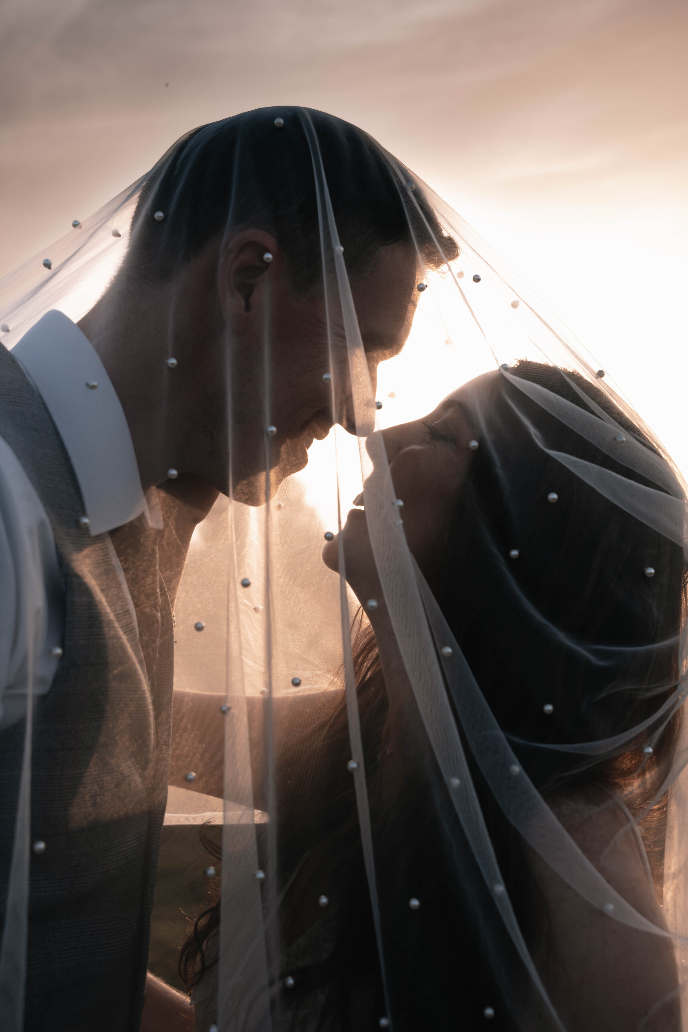 Bride and Groom nose to nose smiling at each other underneath a veil