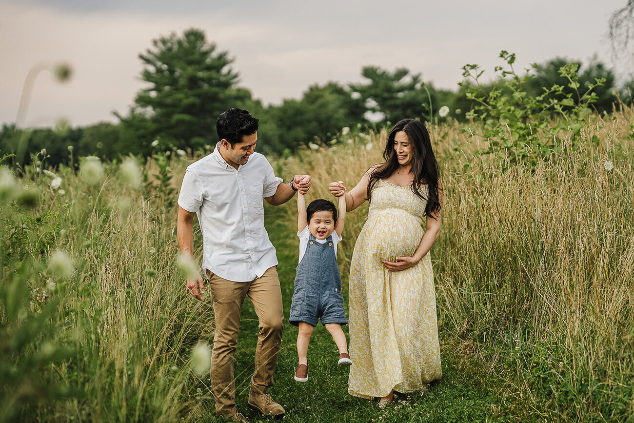 pregnant couple swings toddler son between arms in flower field