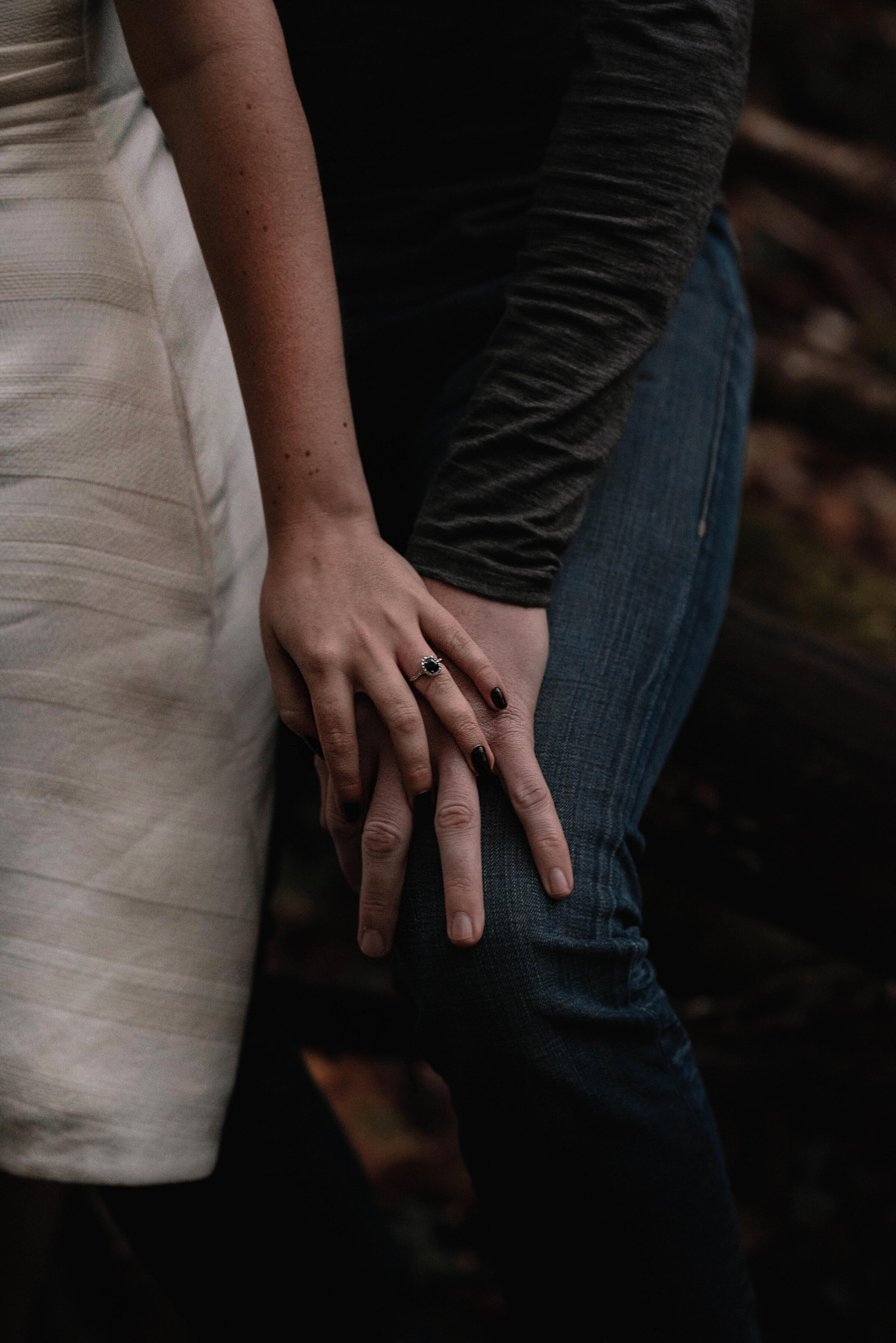 Close up of woman’s hand with engagement ring placed on top of man’s hand which is placed on his thigh