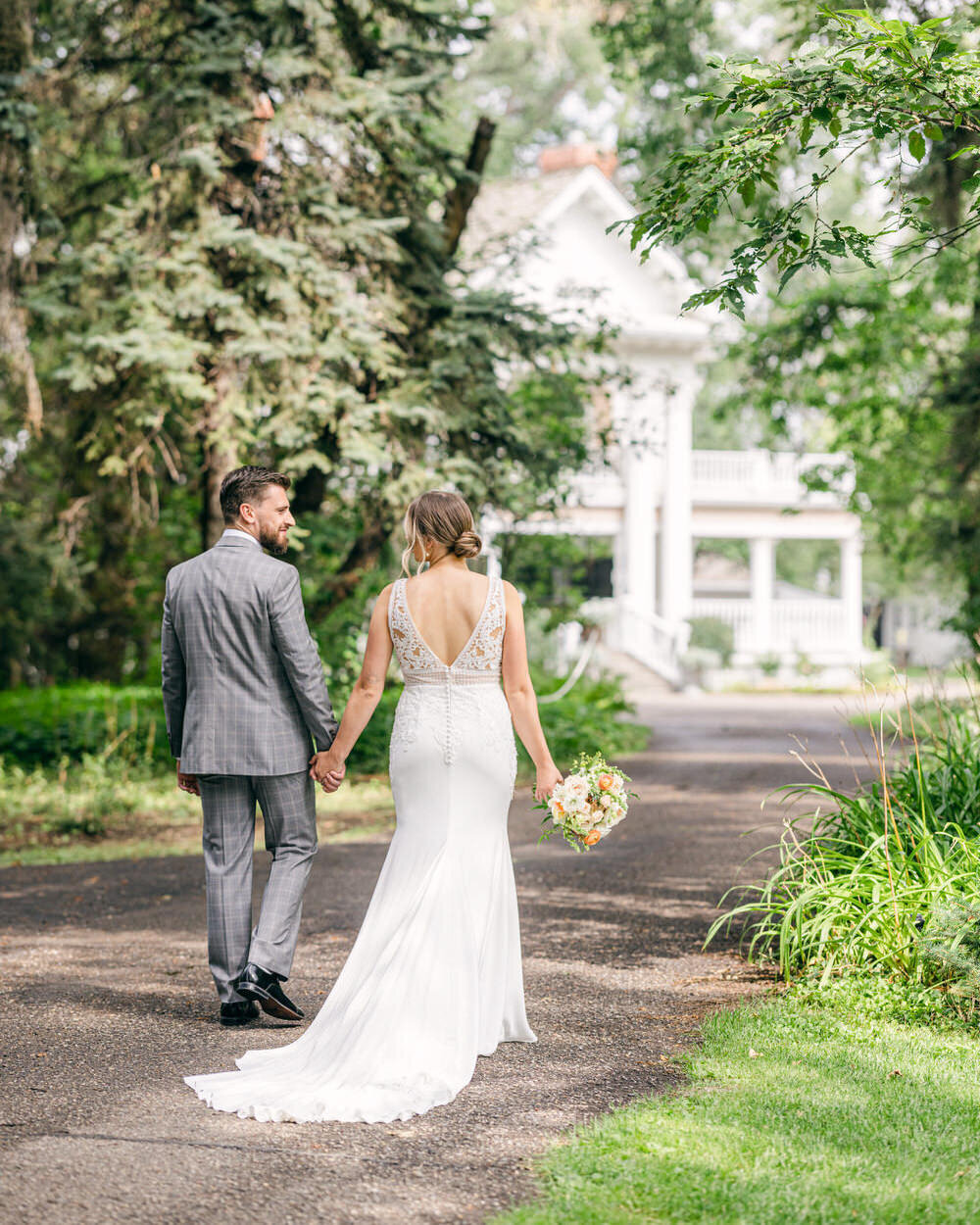 This charming image features the bride and groom taking a leisurely walk along the pathway at the Norland Historic Estate in Lethbridge, Alberta. The lush surroundings and historic backdrop of the estate provide a romantic and picturesque setting for their serene walk together.