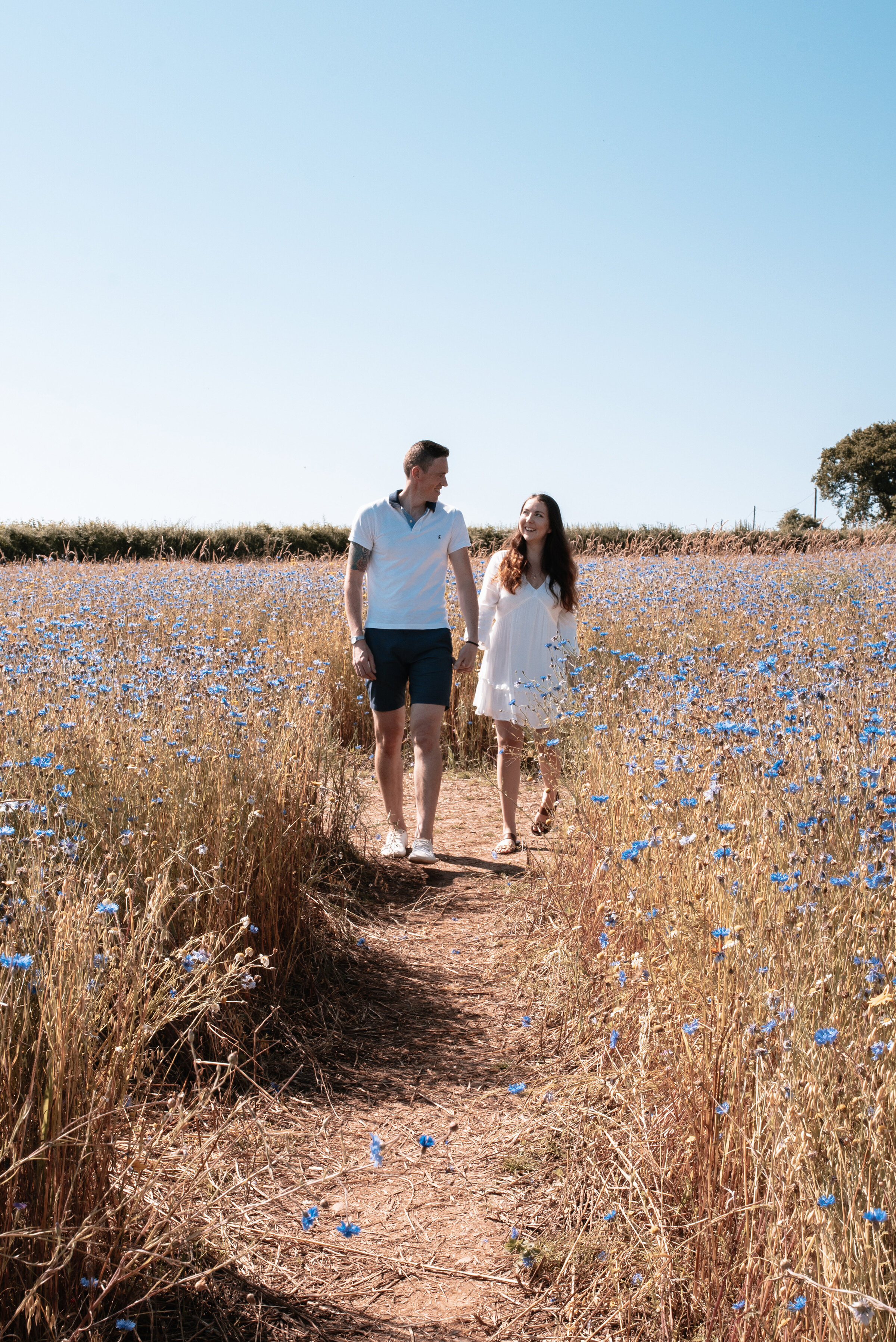 Man and woman laughing and walking hand in hand towards the camera surrounded by wildflowers