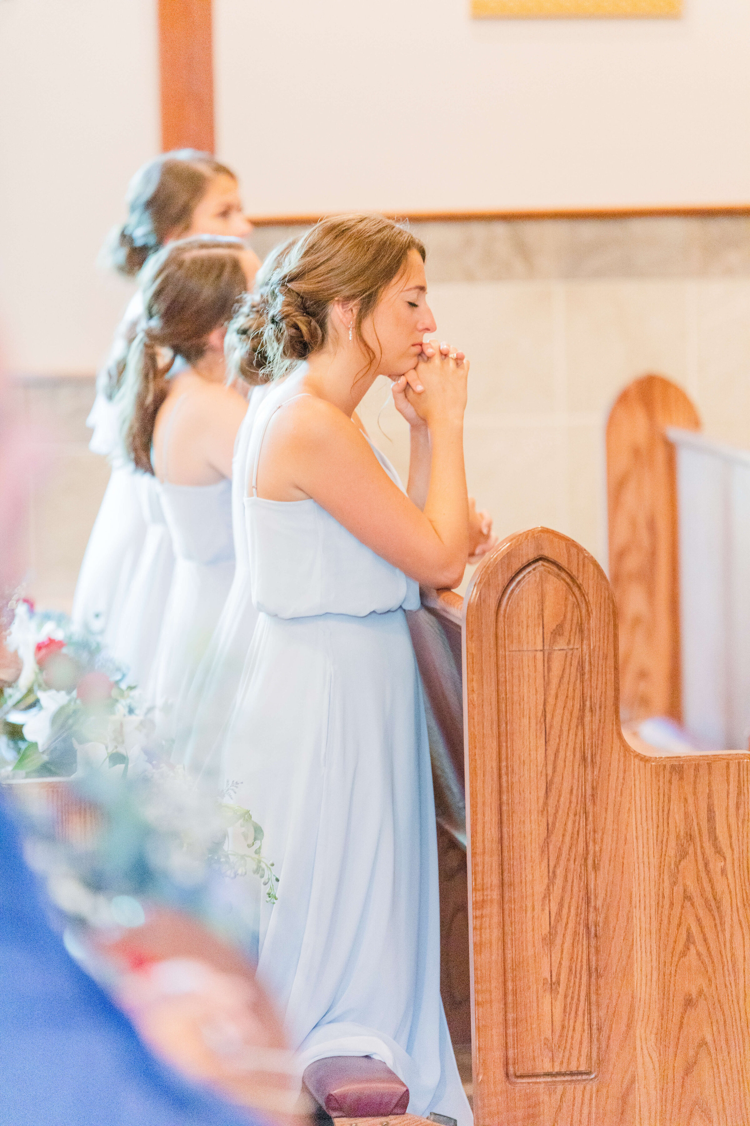 An up close photograph of a bridesmaid in a blue dress praying in church