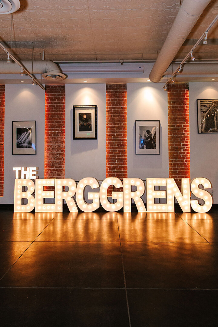 Large marquee letters spelling “The Berggrens” light up against a backdrop of exposed brick at SoHo63, a Chandler wedding and event venue. Framed art and dramatic uplighting complete the stylish indoor setting, perfect for personalized and modern Arizona weddings.