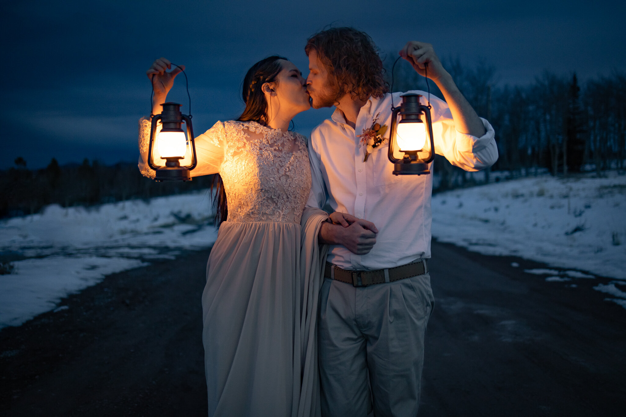 Bride and groom kiss during blue hour while holding up lanterns