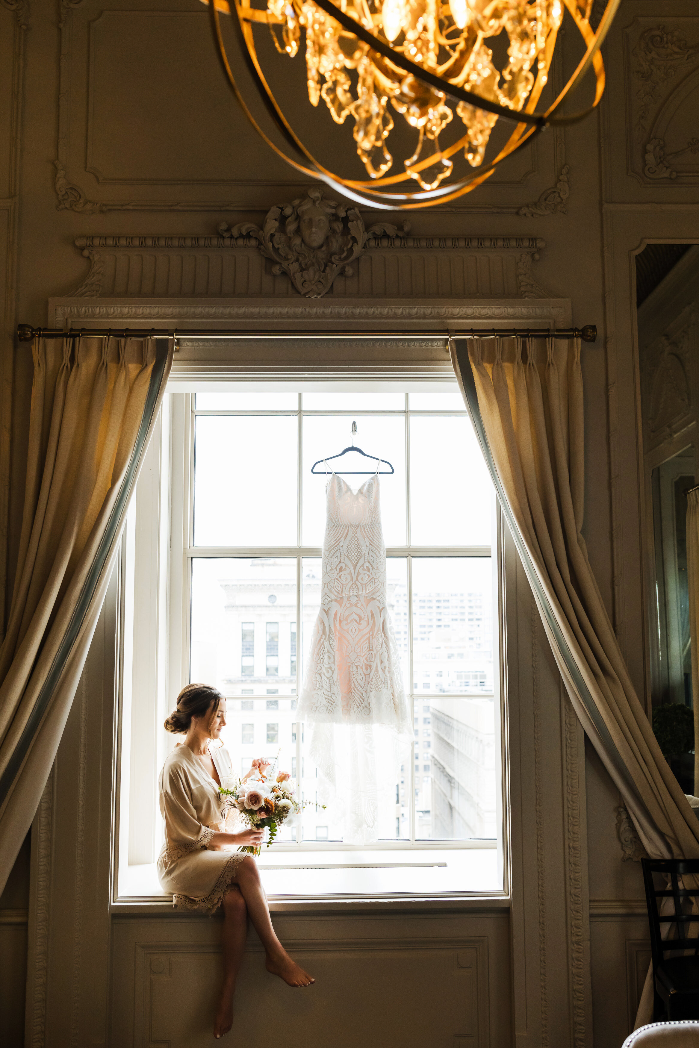 Bride sitting by the window looking at her wedding bouquet  at the Crystal Tea Room Bridal suite in Philadelphia