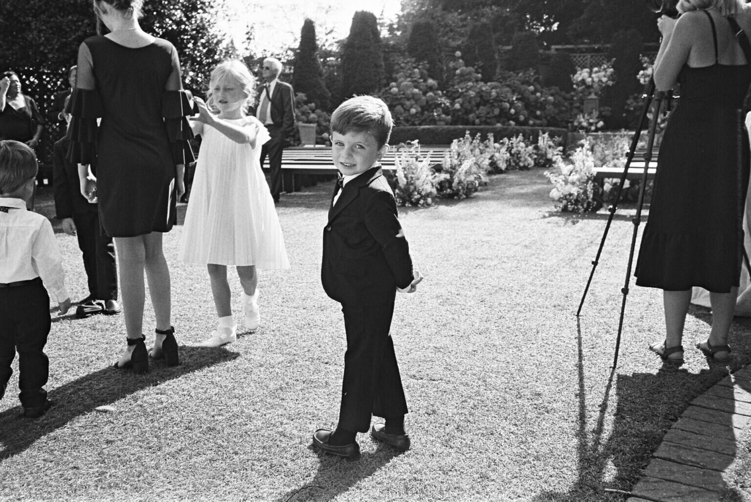 candid black and white photo of little boy in black tux at wedding