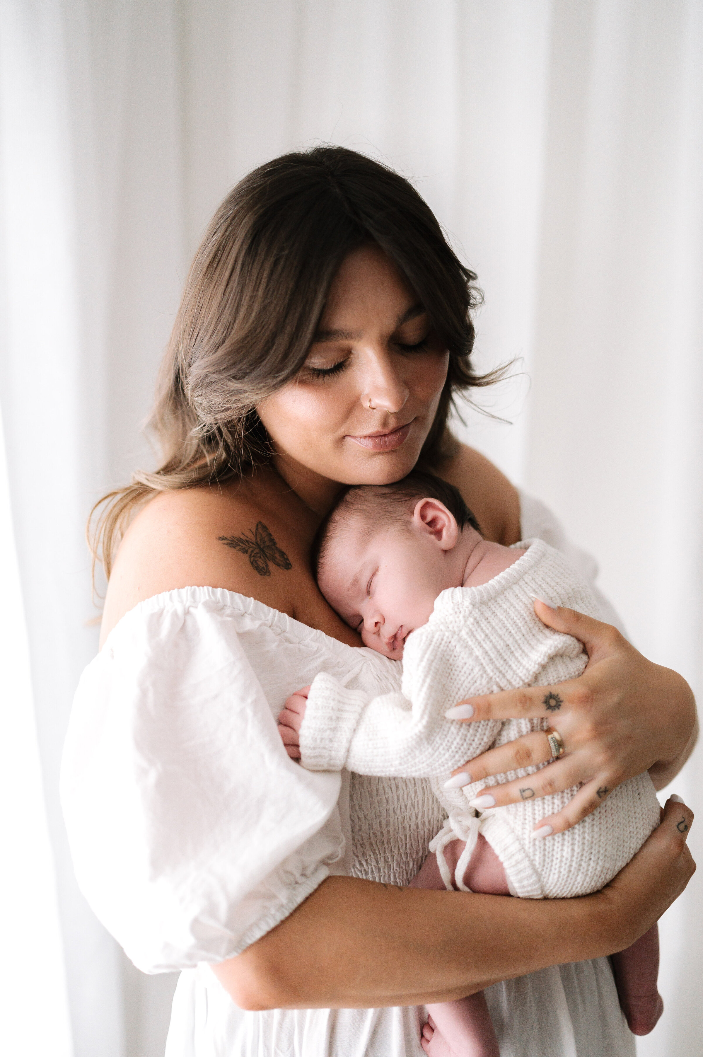 A new mum holding her sleeping newborn daughter on her chest at newborn photoshoot in Billingshurst