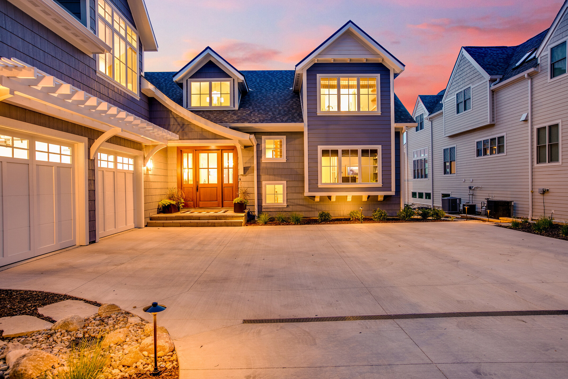 A captivating nighttime view of a custom home entryway, illuminated by warm interior lights. The stunning backdrop of a purple and pink sunset enhances the home's inviting and luxurious atmosphere.