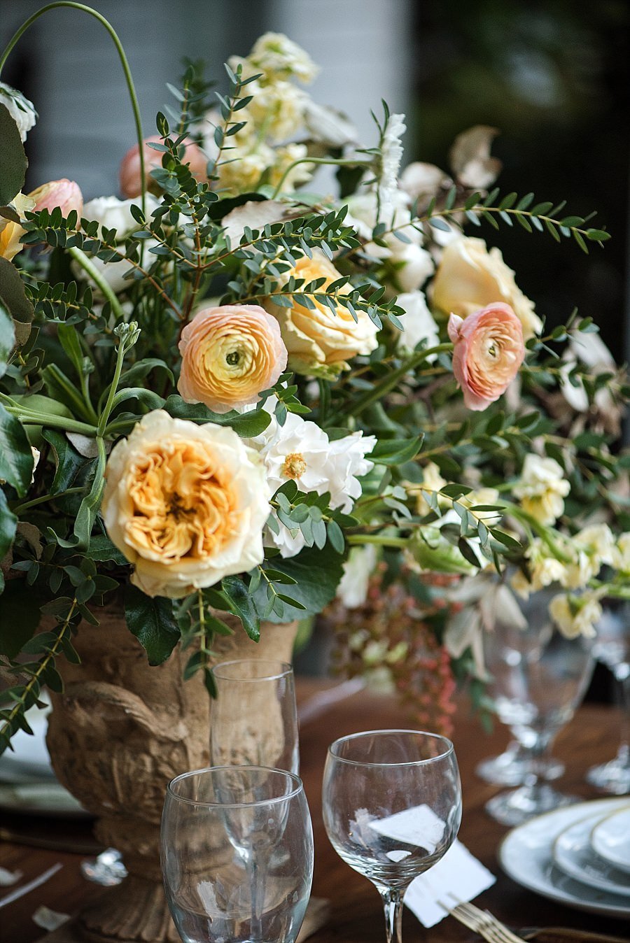 Orange, yellow and cream colored flowers in a tall compote