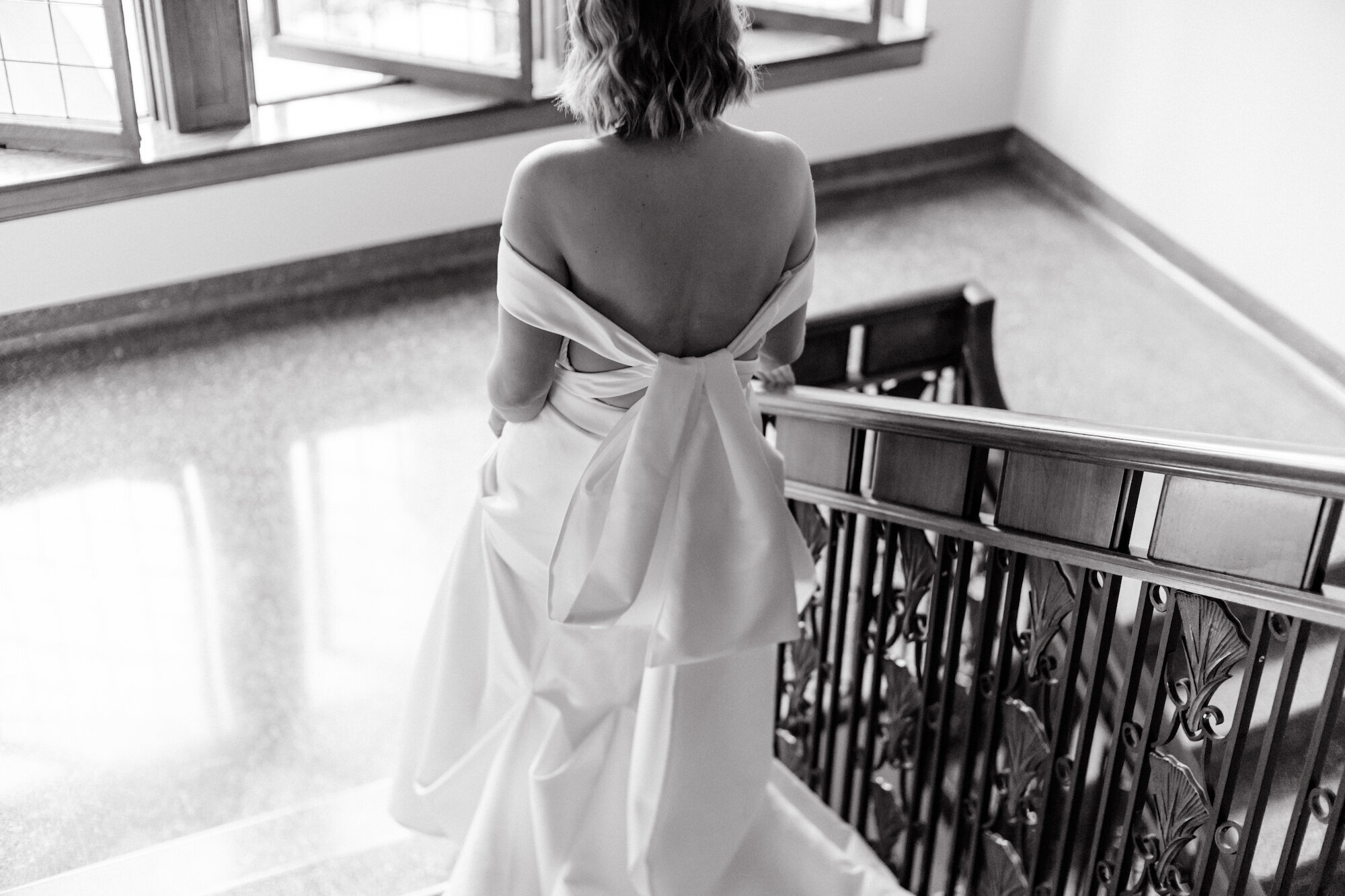 black and white photo of bride walking down the stairs in an off the shoulder gown