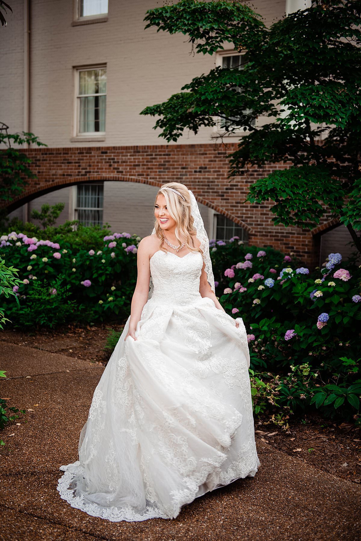Bride wearing Cinderella ballgown standing in outdoor courtyard at the Gaylord Opryland with pink, purple and blue hydrangeas behind her