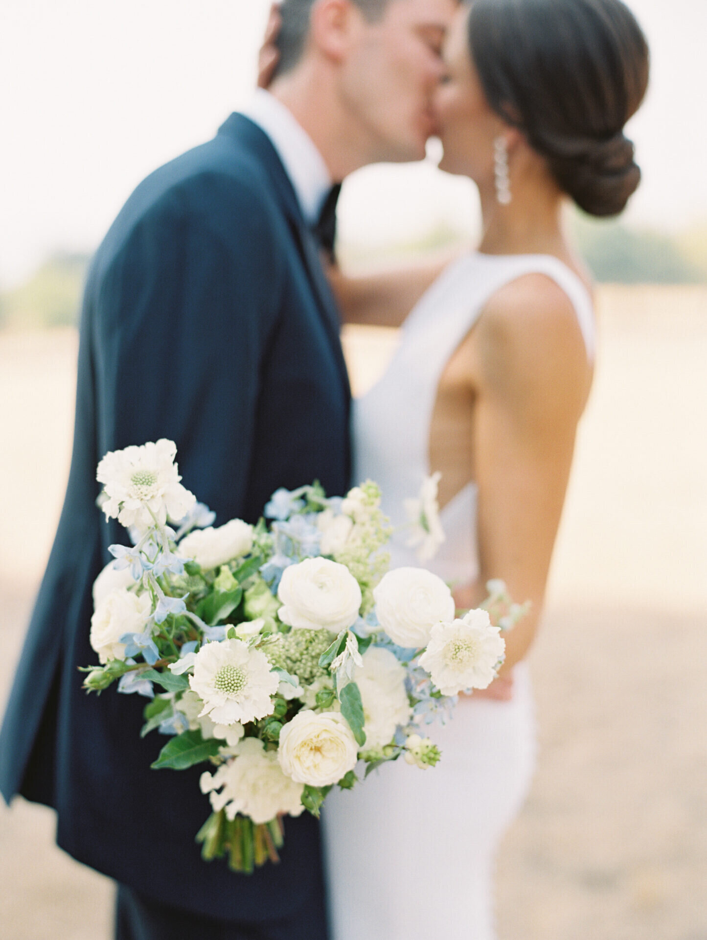 white and green bridal boquet with couple kissing in background