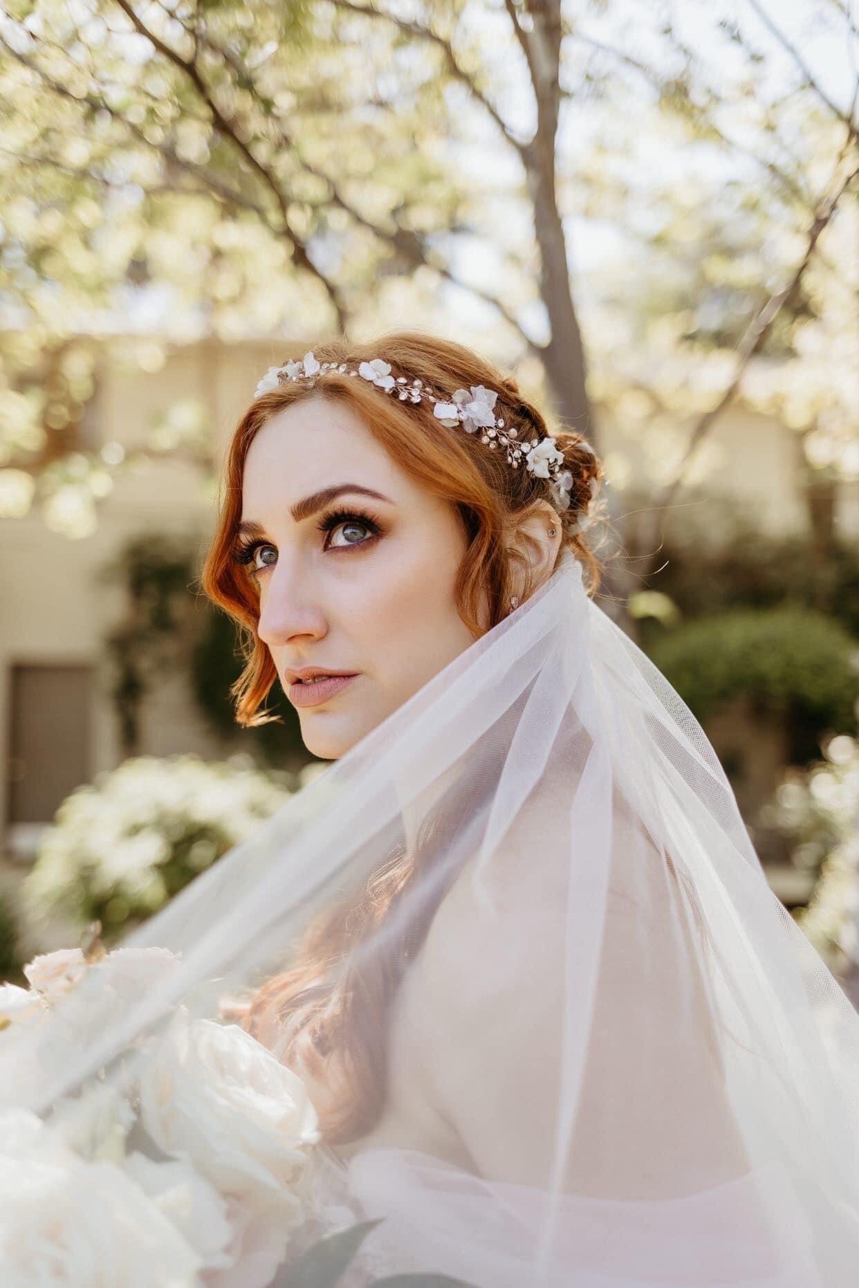 A red-haired woman  wearing a wedding dress. A wedding veil covers her shoulders