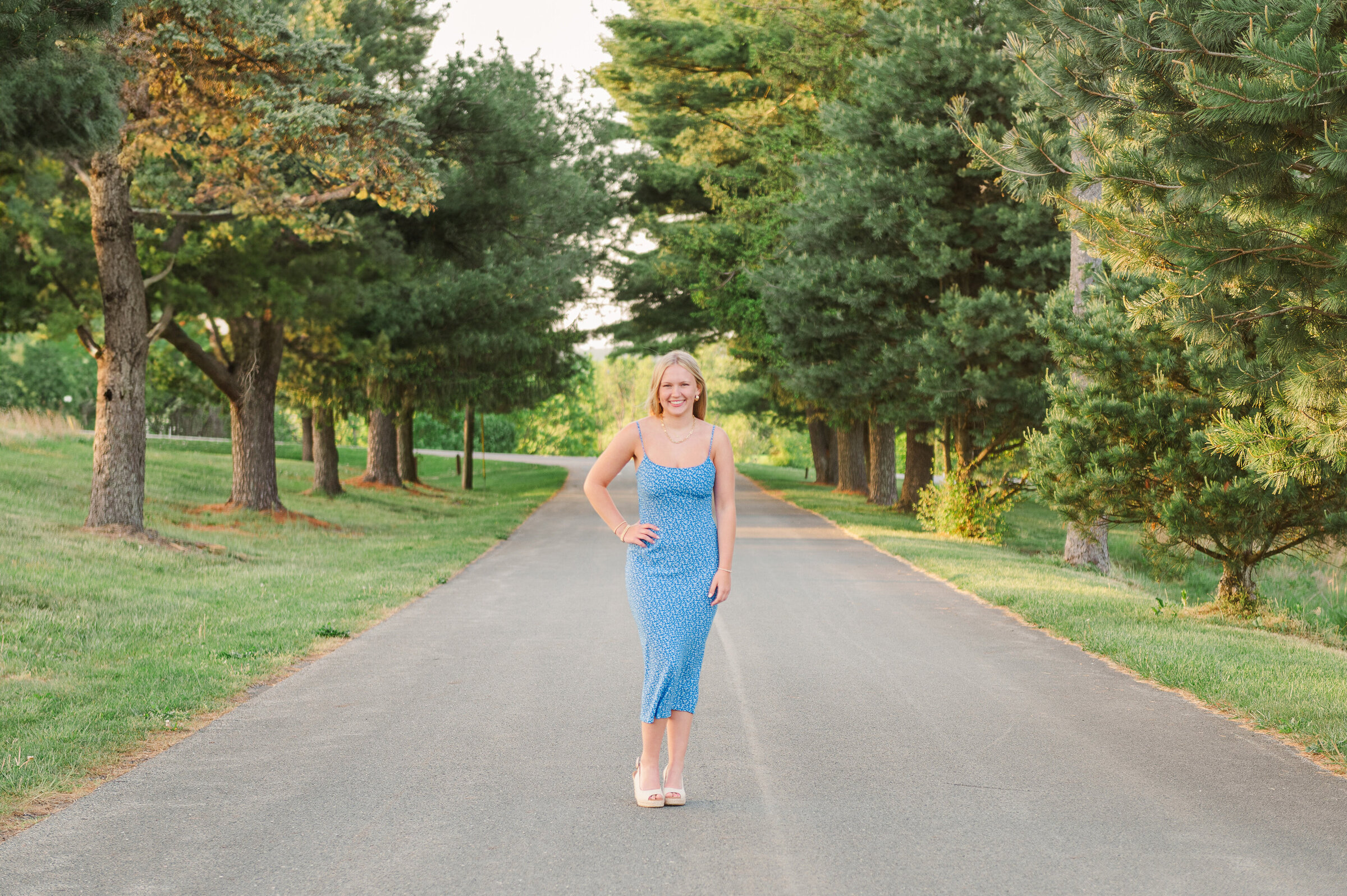 Senior girl in blue dress, standing in the middle of a road surrounded by trees by York PA photographer