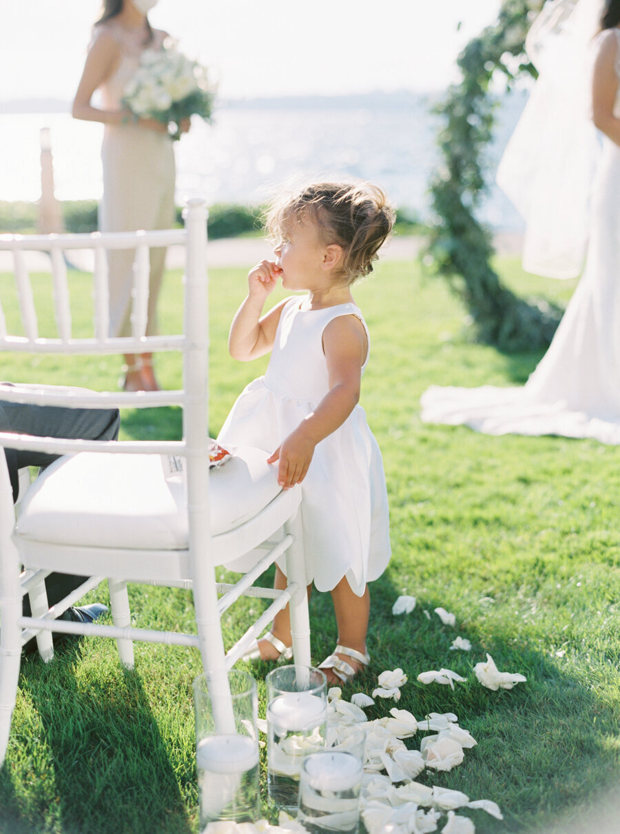 flower girl in white dress on sunny grass at lake front wedding