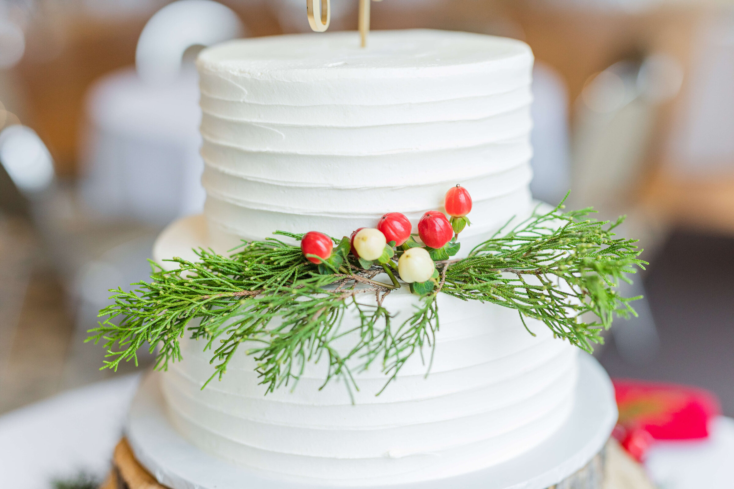 An up close photograph of a white wedding cake and green christmas garland and white and red little buds