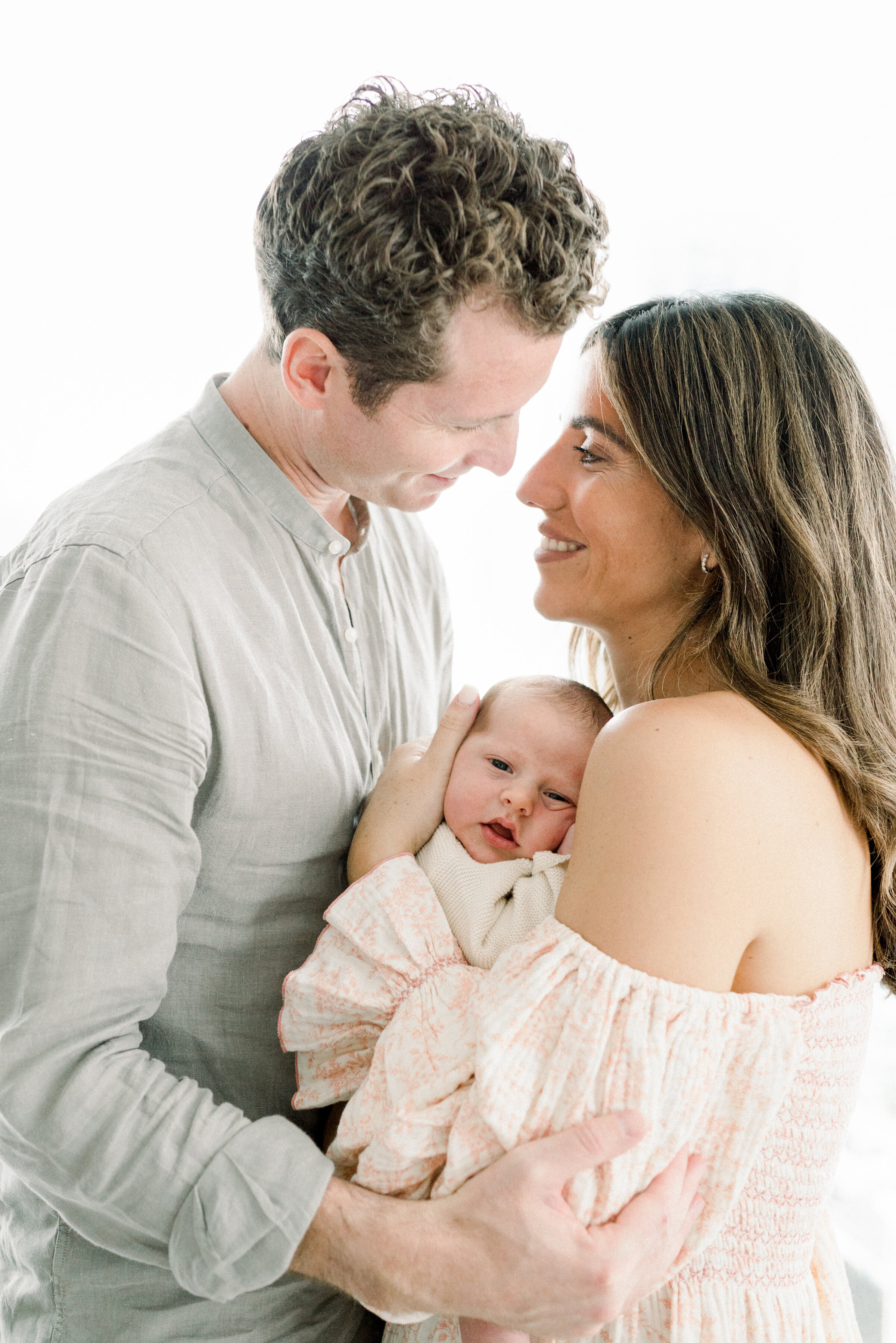 Dad and mom looking at each other while newborn looks at camera by Miami Newborn Photographer