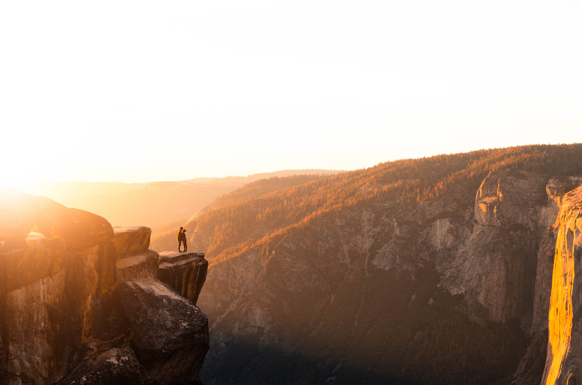 couple standing on edge of mountain cliff at sunset