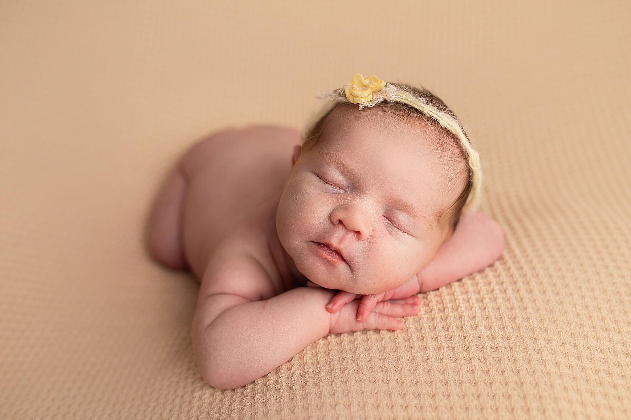newborn baby laying on yellow blanket on her belly