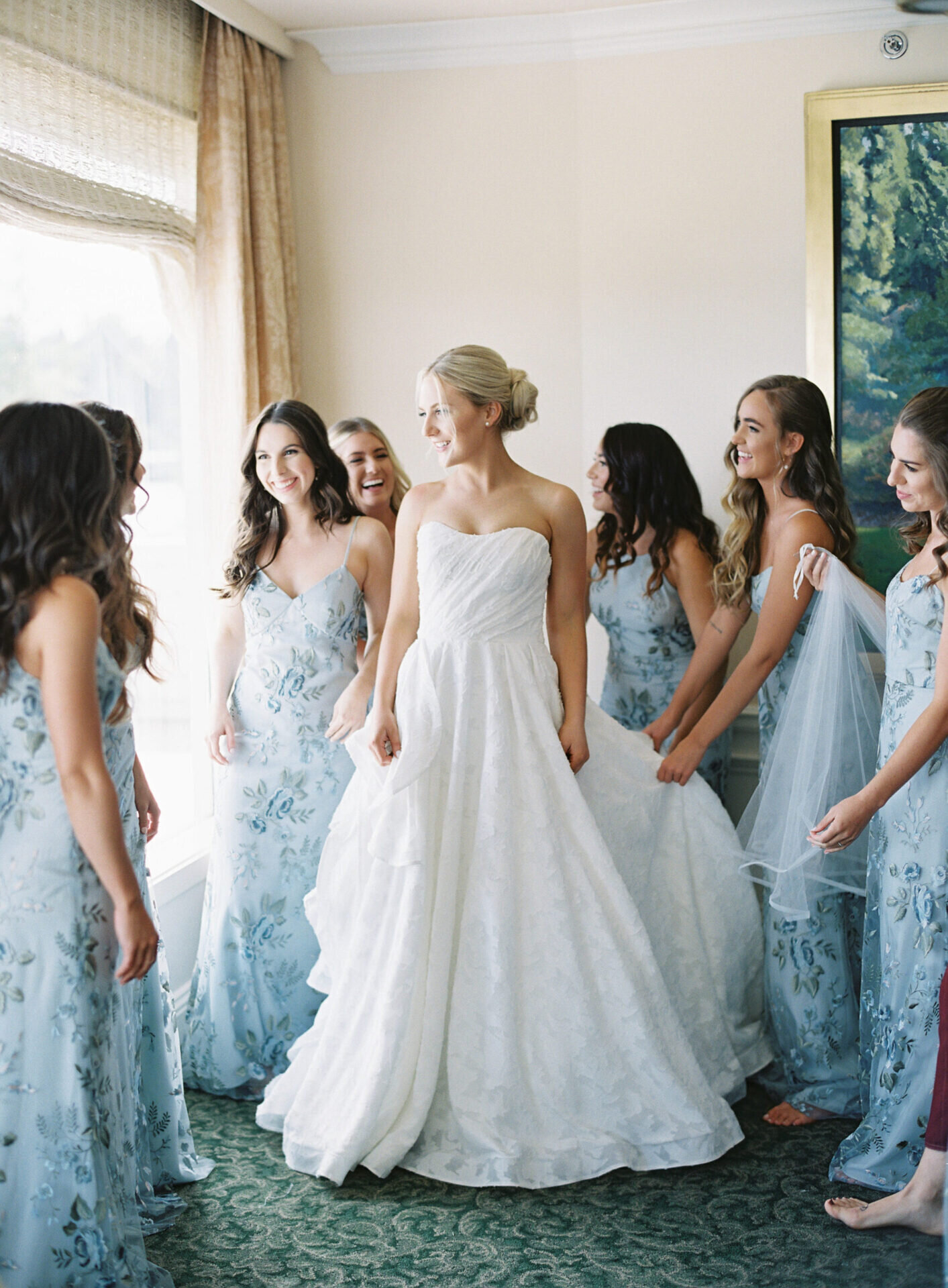 bride with bridesmaids in long light blue gowns helping her get ready