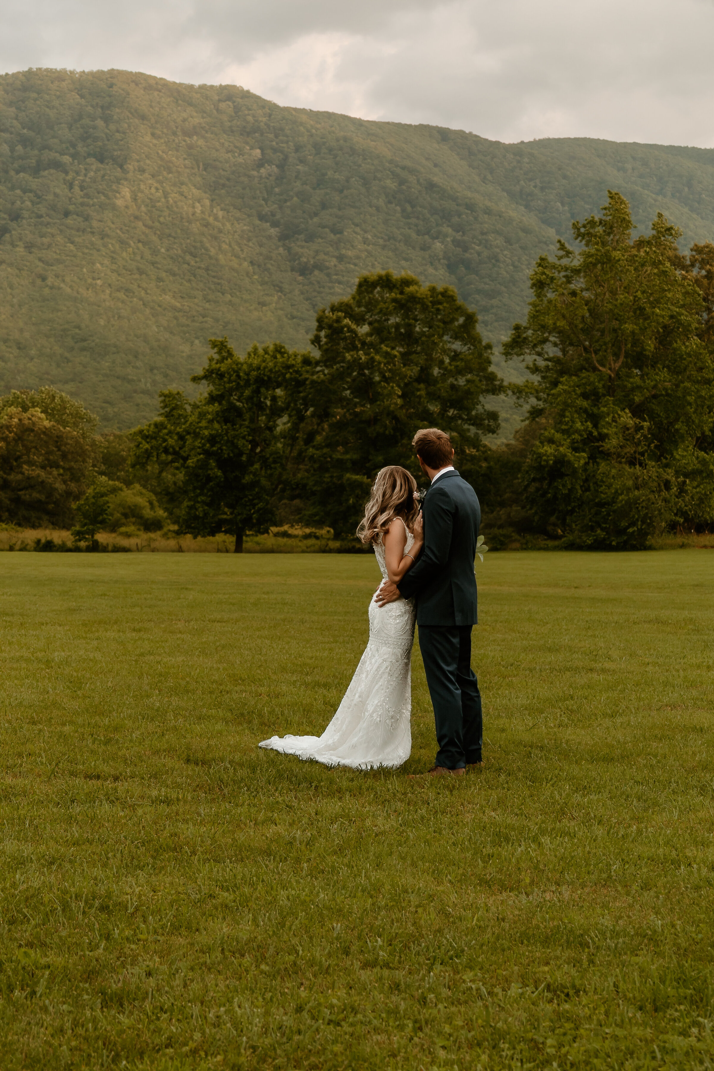A bride and groome facing eachother in a field with a rustic mountain scene in the distance