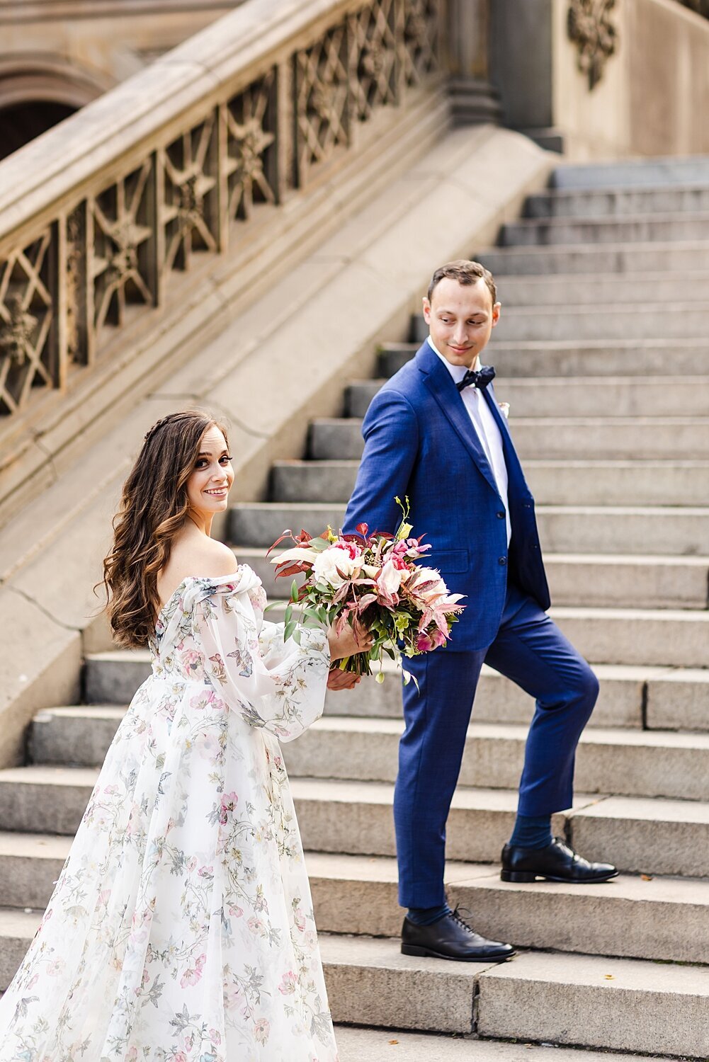 Groom holds bride's hand as they walk up the stairs in Central Park in New York City, New York