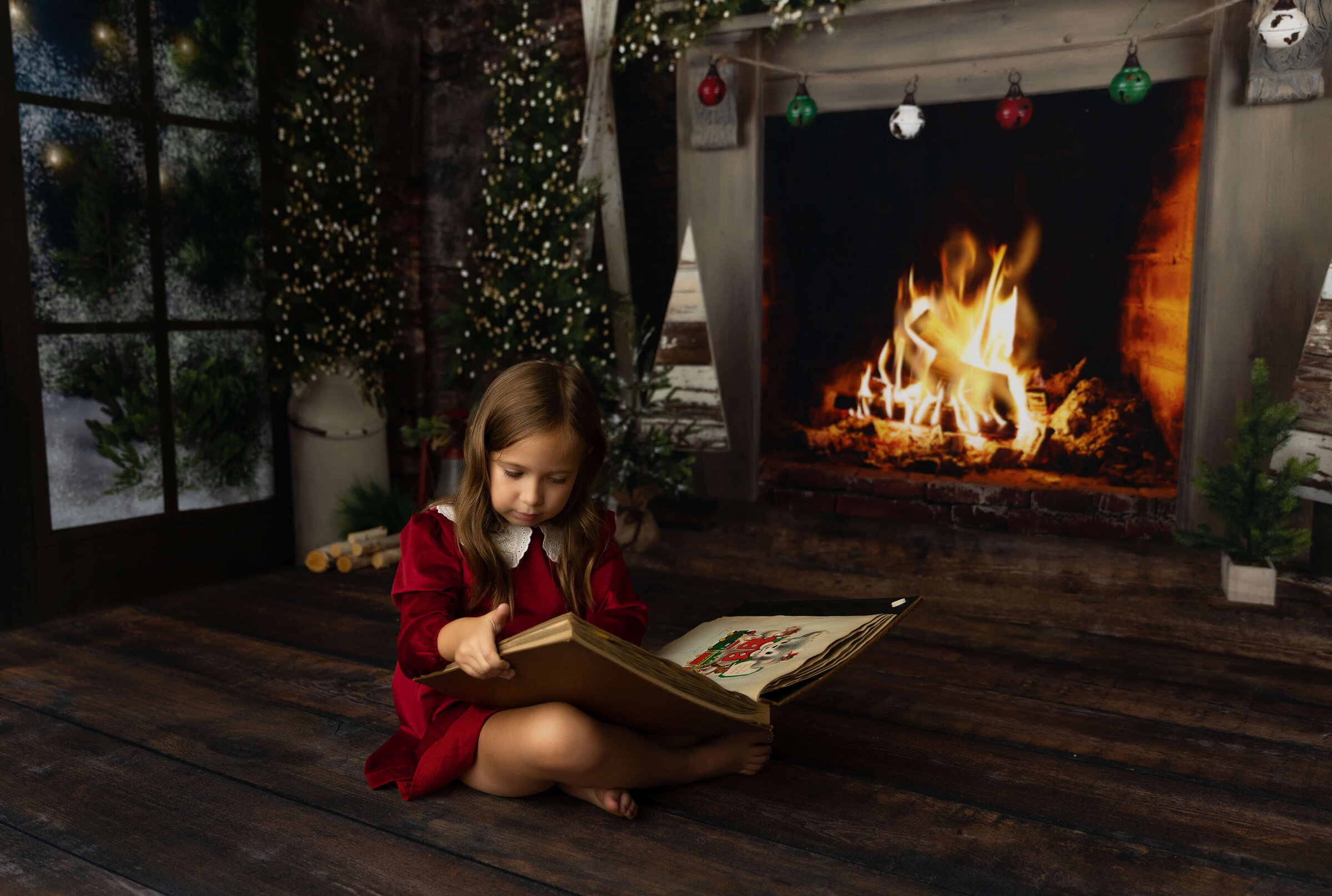 Christmas photo of a little girl reading a book by a fire