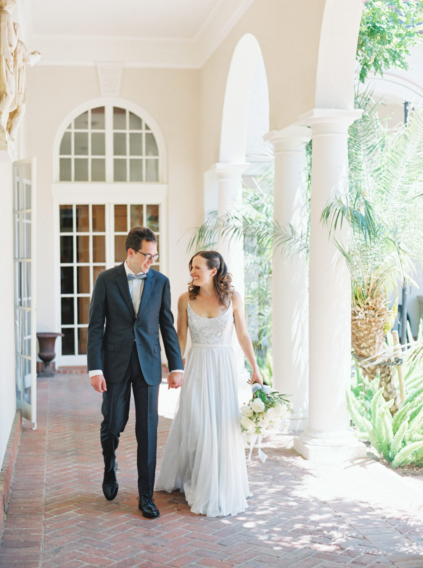 bride in light blue flowy dress holding hands with groom in navy suit