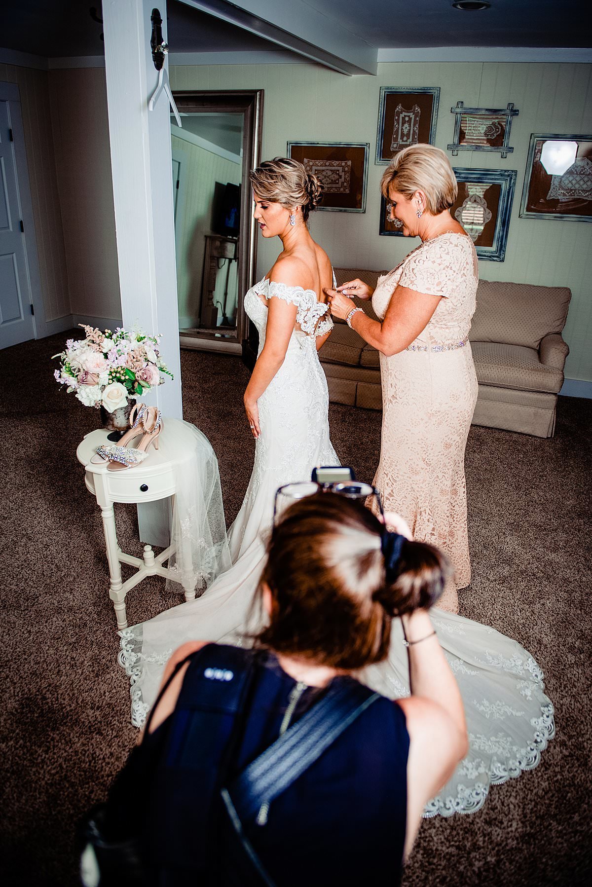 Behind the scenes photo of photographer taking pictures of brides mother buttoning up her dress in the bridal suite at Saddlewoods Farm