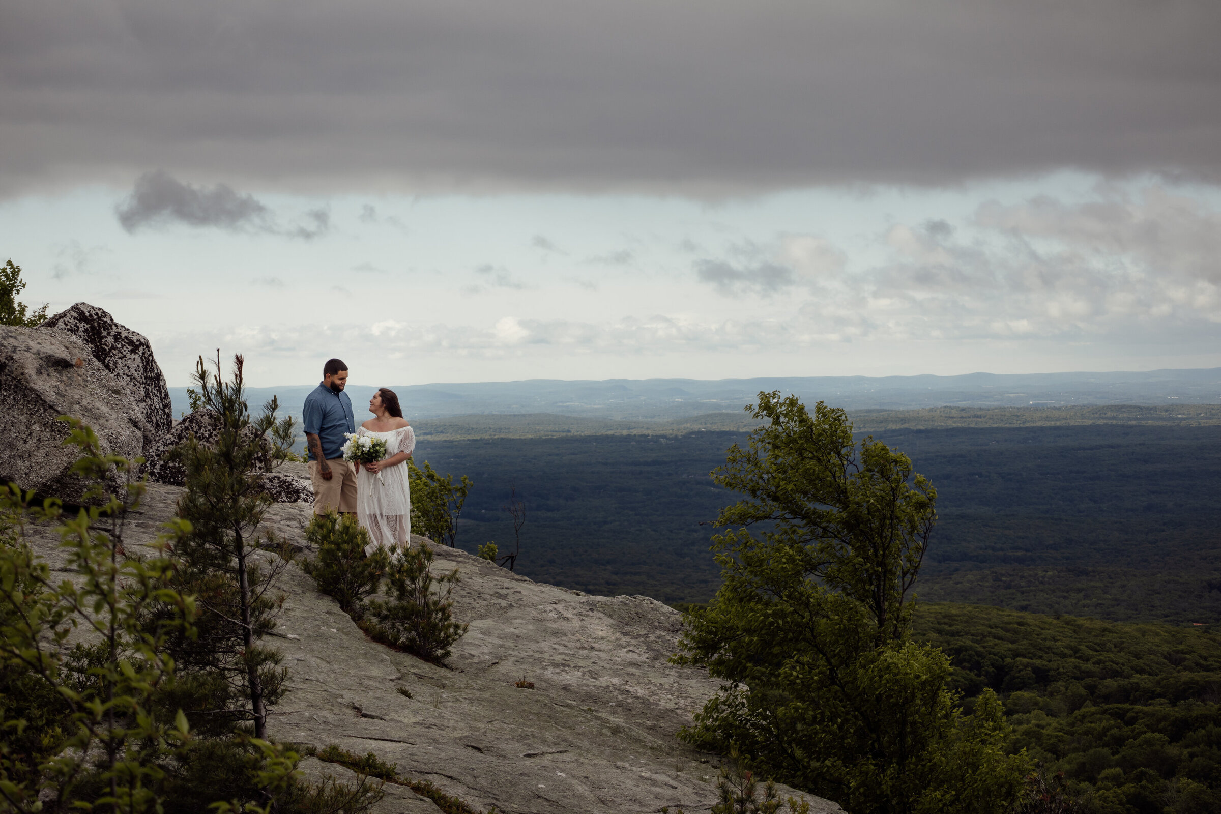 Bride and groom are posing for portaits on top of a mountain with the rolling valleys in the background