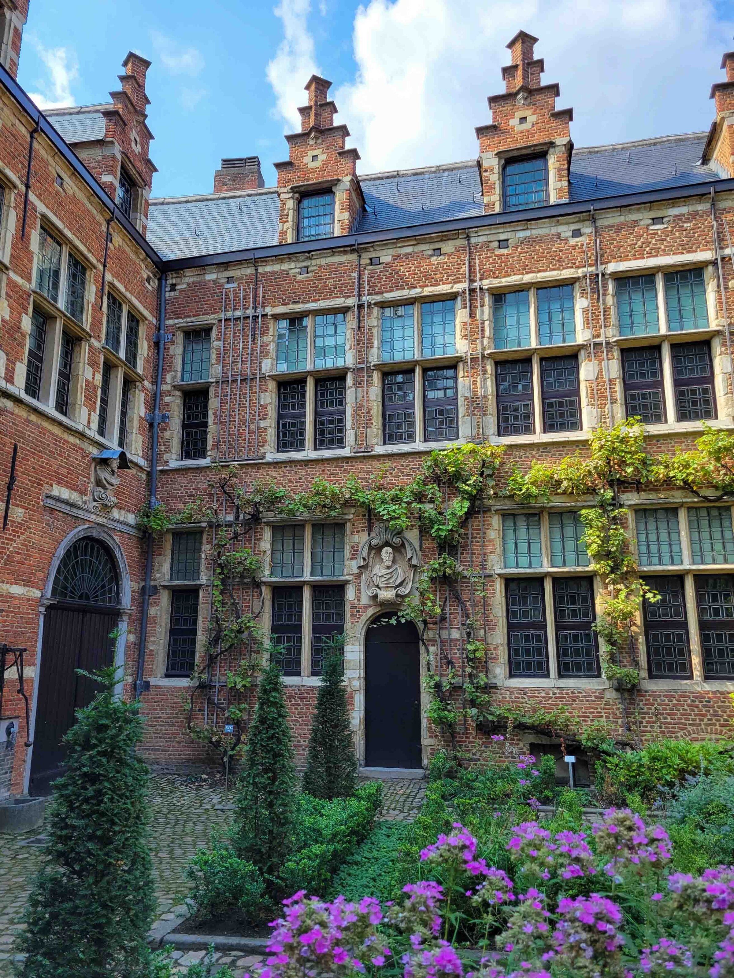 A courtyard at the Plantin-Moretus Museum in Antwerp, Belgium, with typical Flemish brick architecture and purple flowers ©Stephanie Dosch | theViatrix Luxury Travel