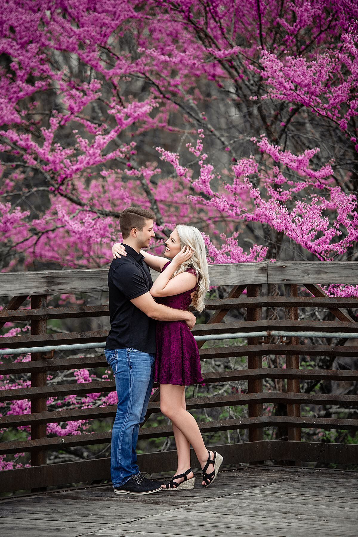 Engagement photo of couple standing on deck near flowering pink trees