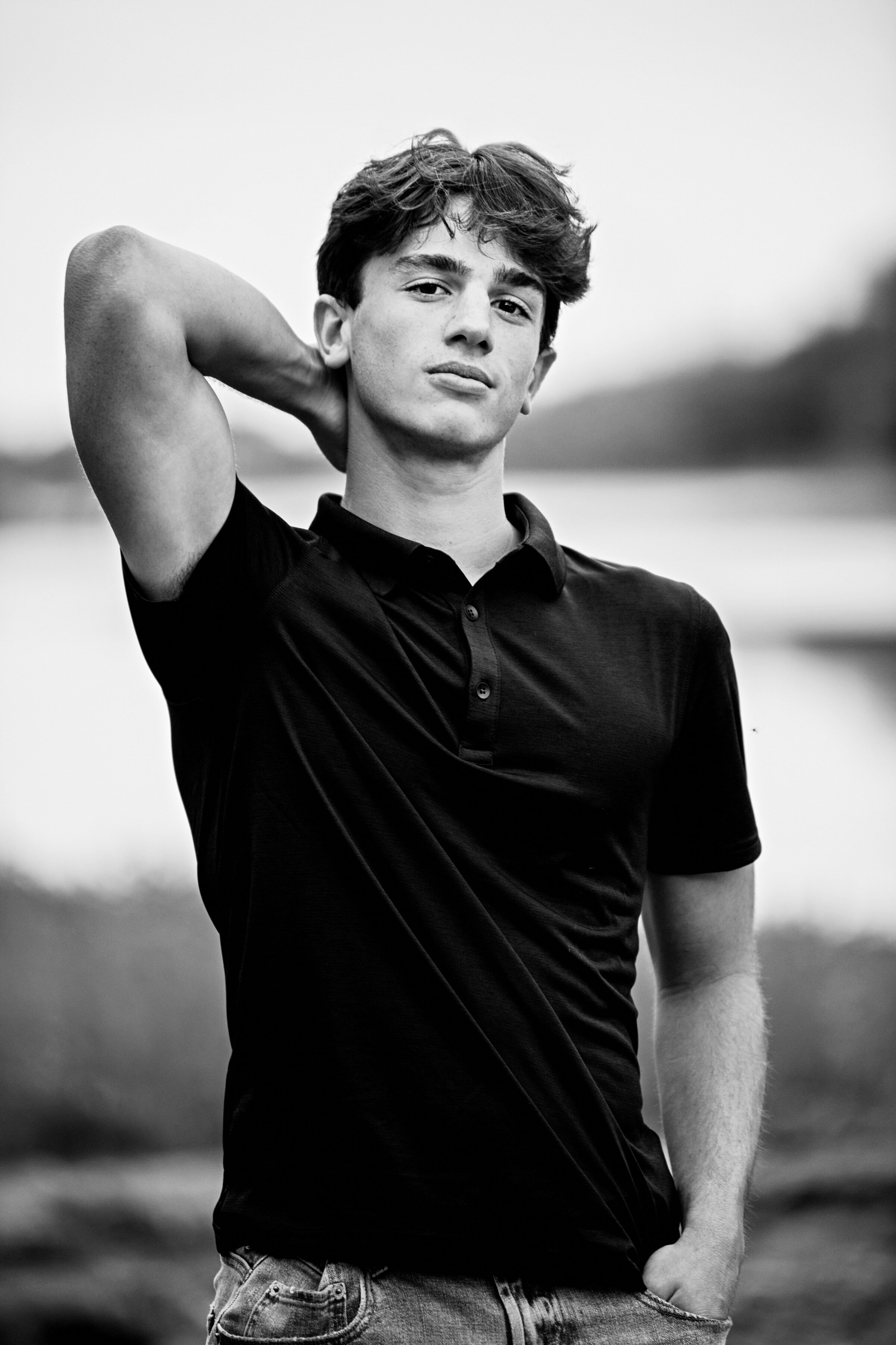 high school senior photo of boy in black and white  wearing black t-shirt  in front of river in Minnesota