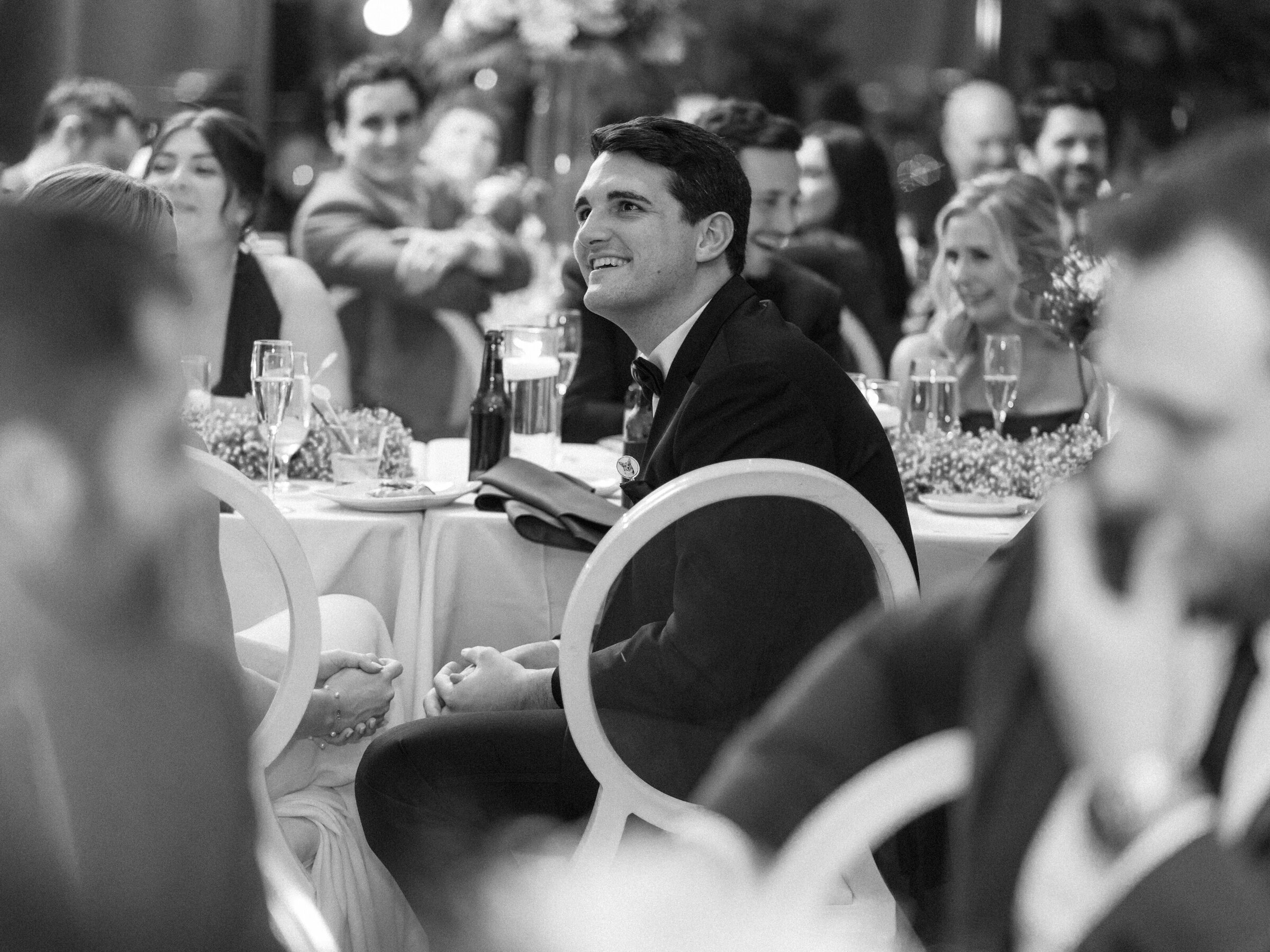 A groom smiles and laughs during toasts at their wedding reception in Cincinnati, Ohio.