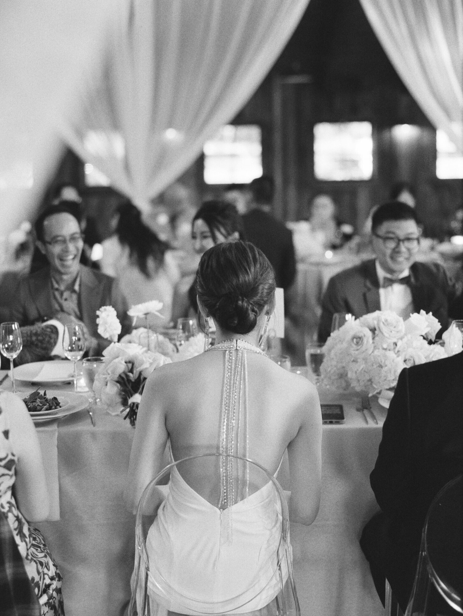 back of the bride as she sits at her reception in ghost chair black and white