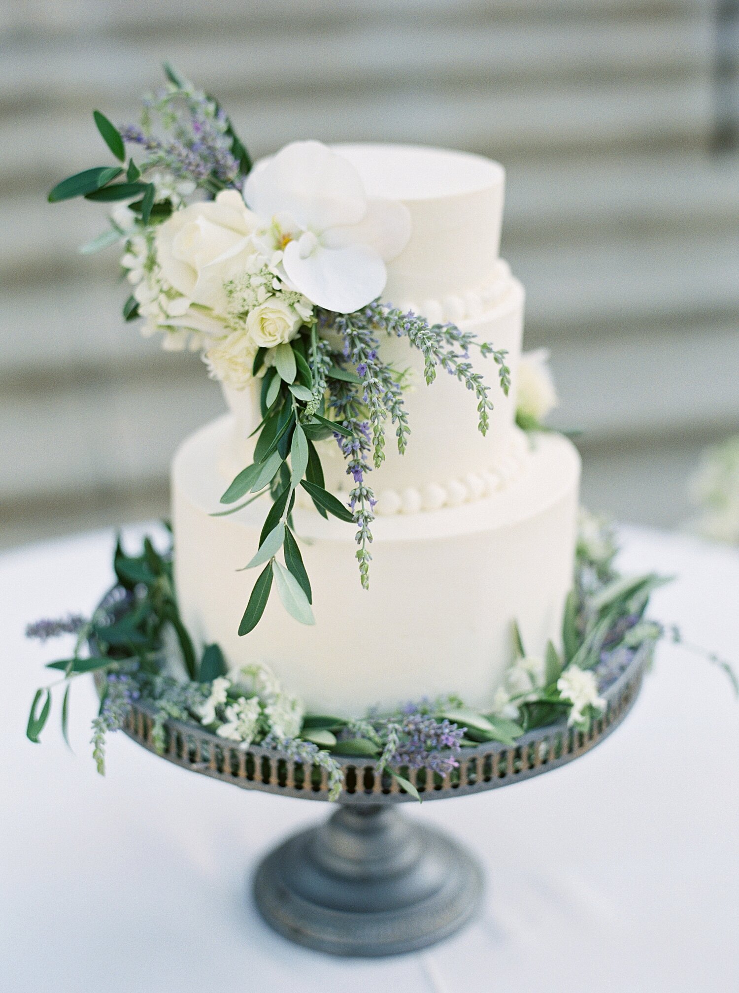 white three tiered cake with lavender and eucalyptus flowers adorning it