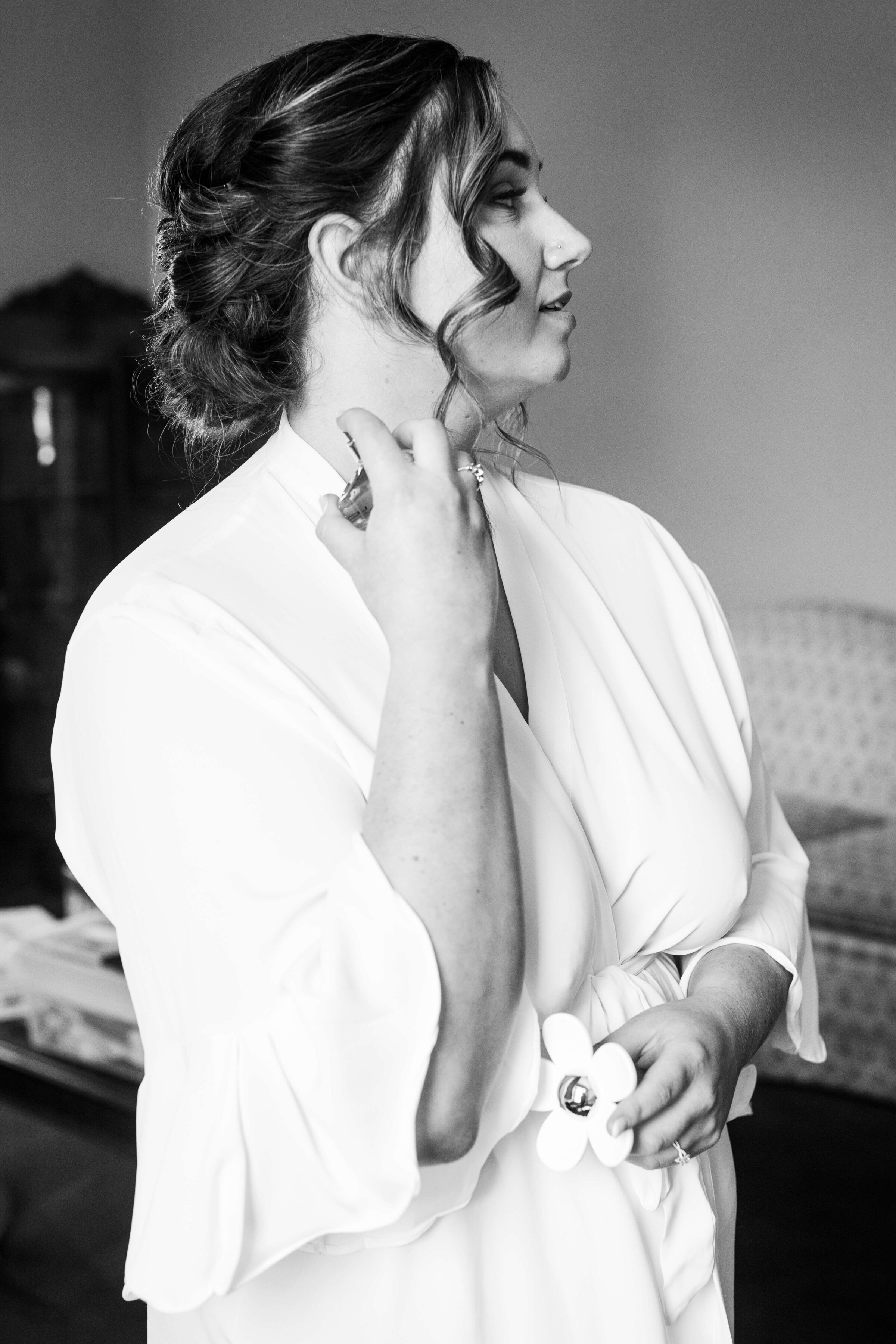An up close black and white photo of a bride putting on perfume in her white robe