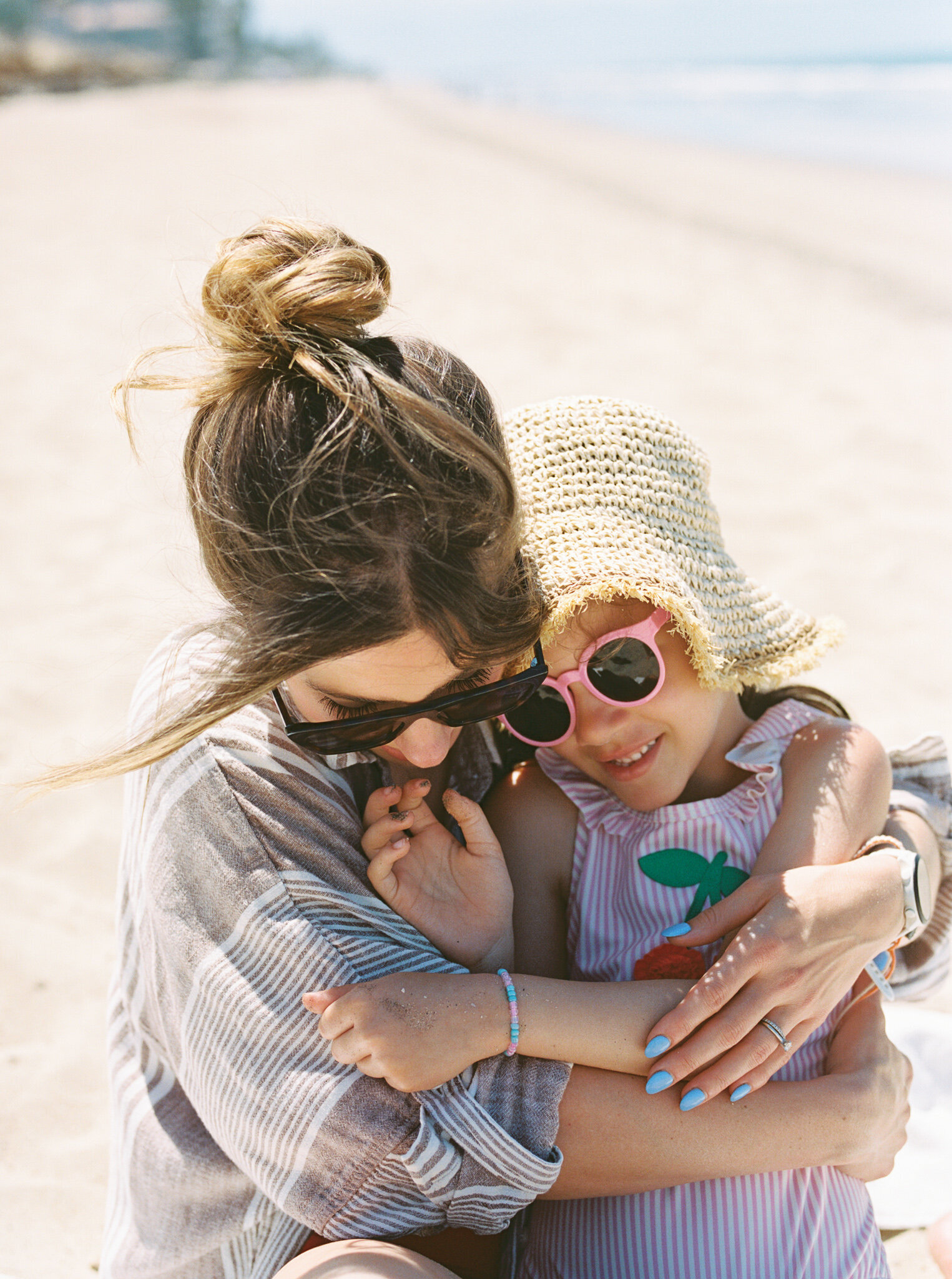 Little Rock photographer Bailey Feeler wraps up her young daughter that is wearing a sun hat and sunglasses, while sitting on the sand of a Mexican beach.