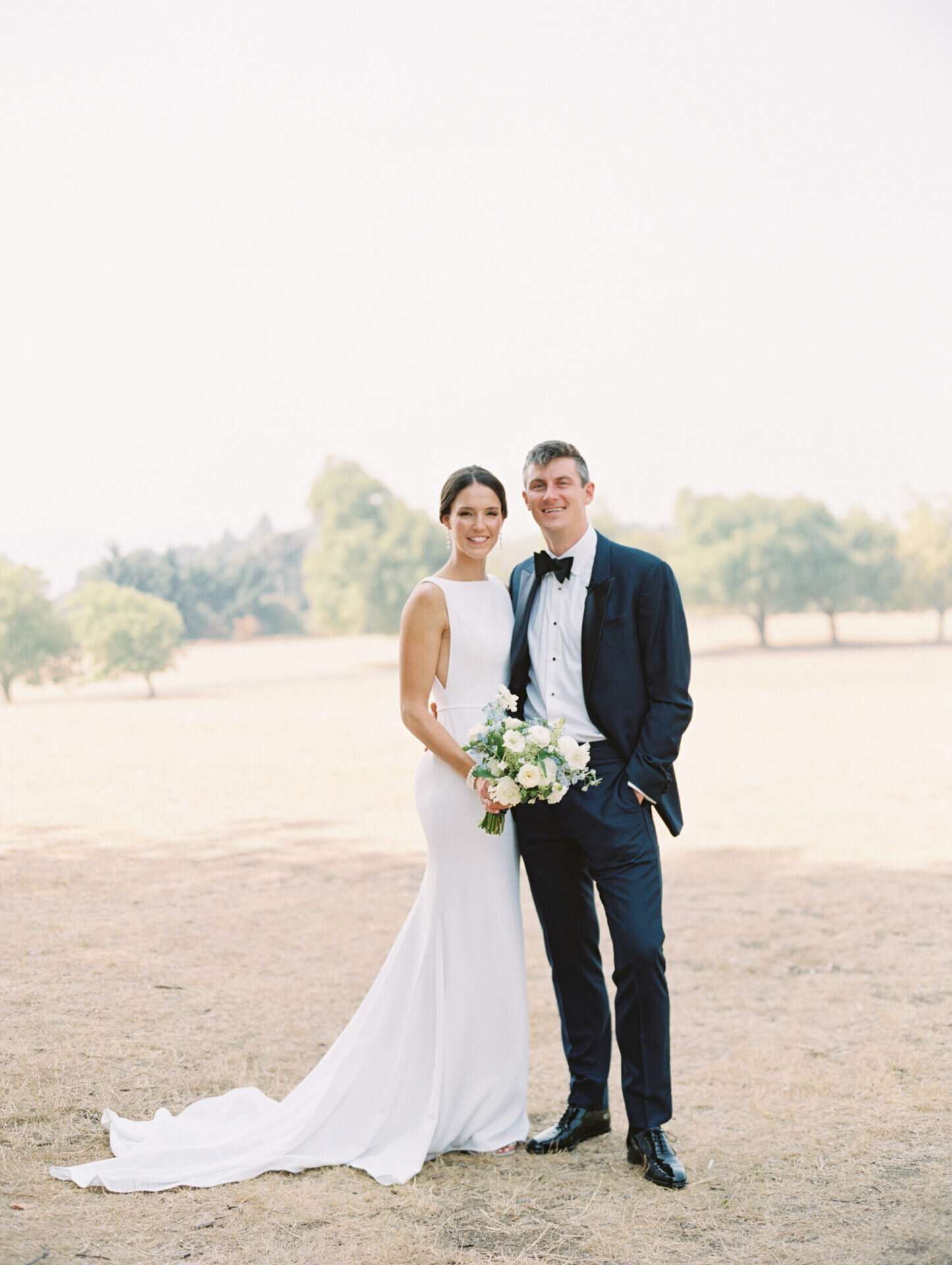 bride and groom smiling at camera at park with soft tones and pastel colors