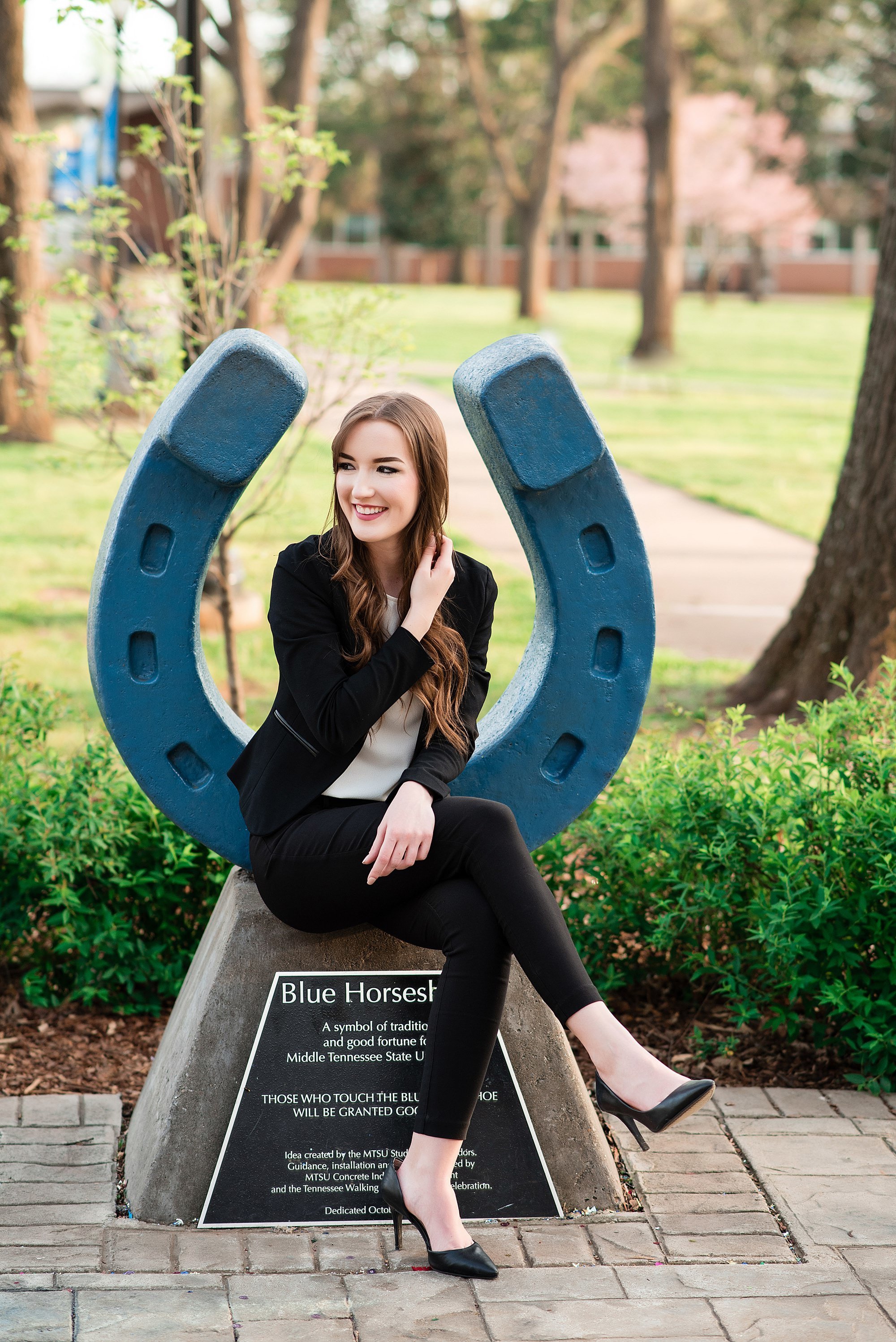 College senior wearing a black suit and black stilettos sitting on the horseshoe at MTSU