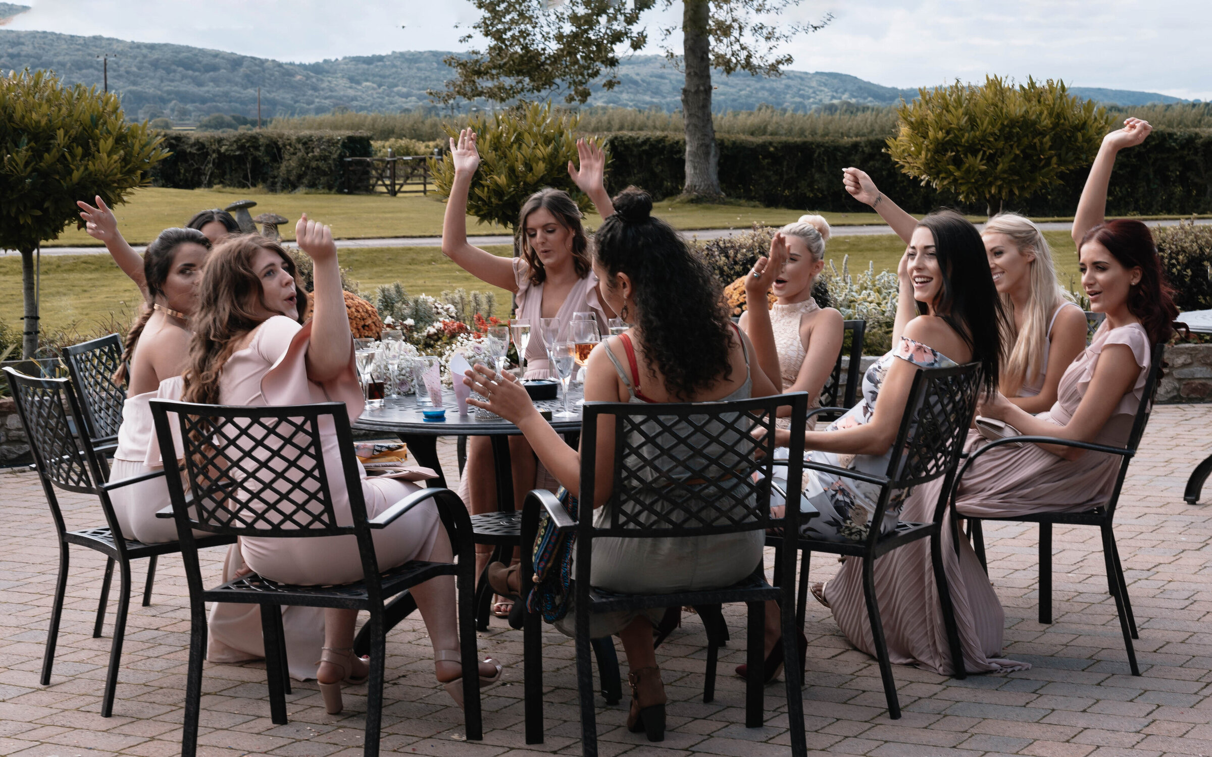 Bridesmaids and friends seated on garden furniture cheering and raising their hands