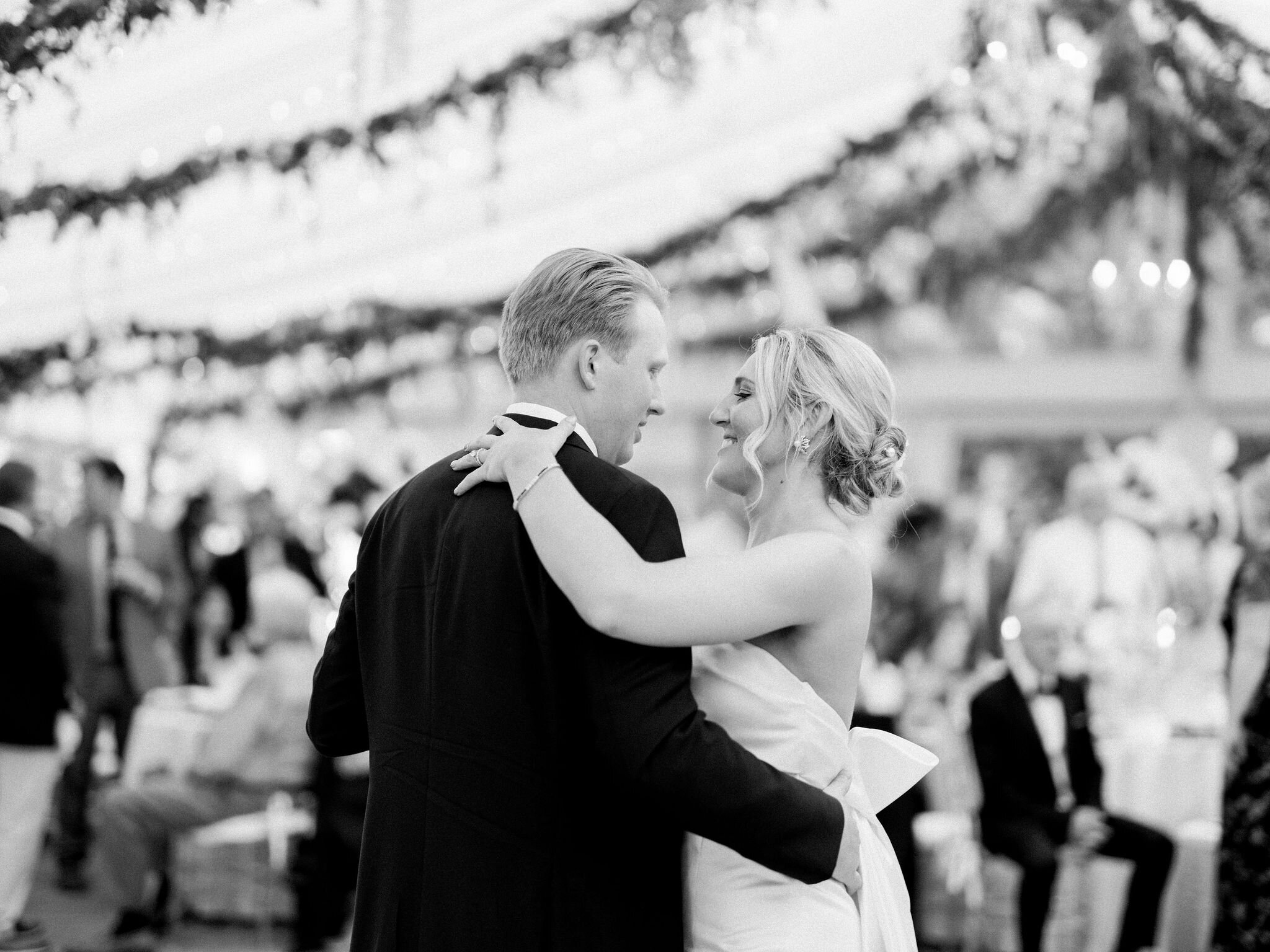 Black and white photo of a couple sharing their first dance beneath a tent of hanging greenery