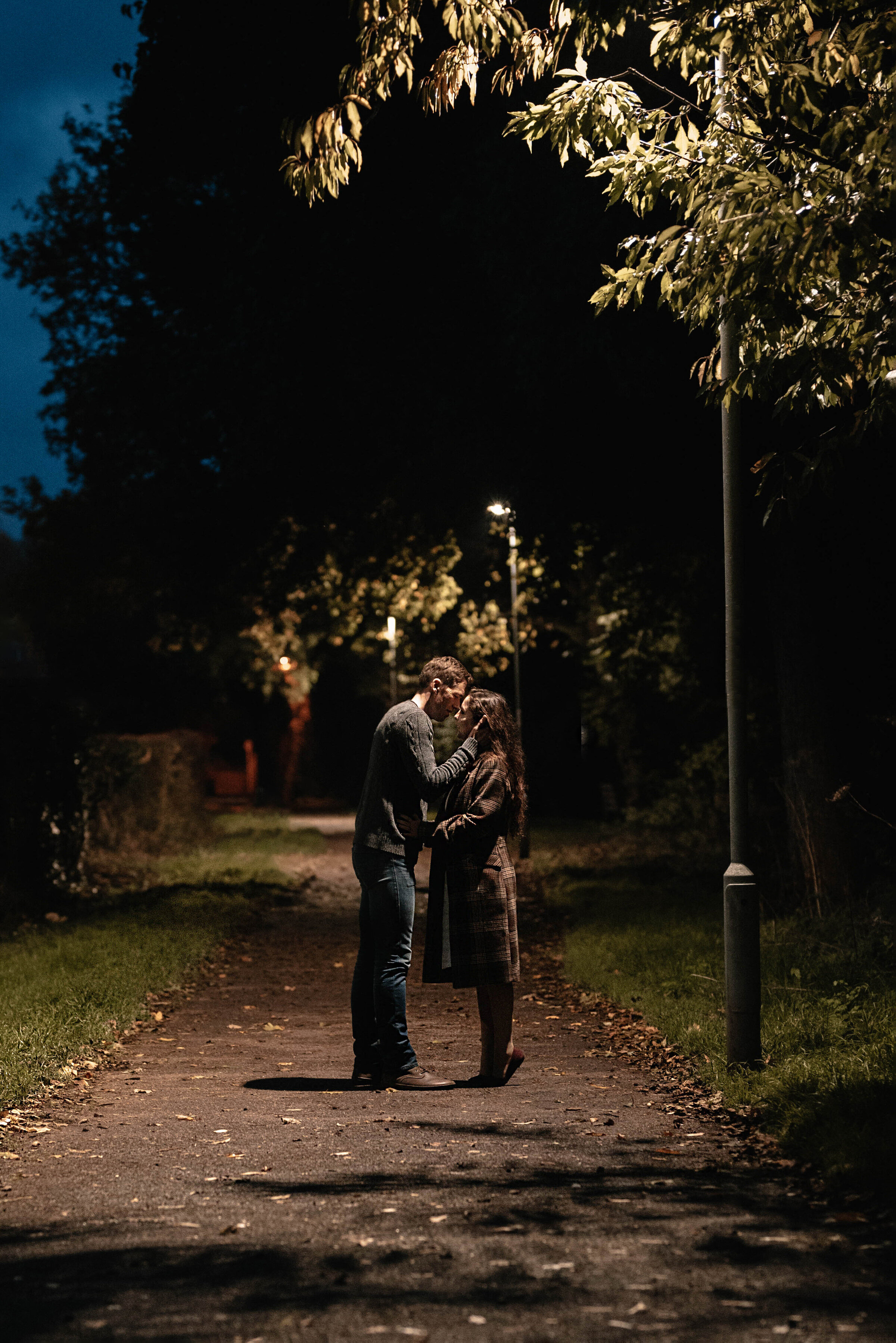 Man and woman kissing beneath a single lamppost, she is on tip toes and he is running his hands through her hair