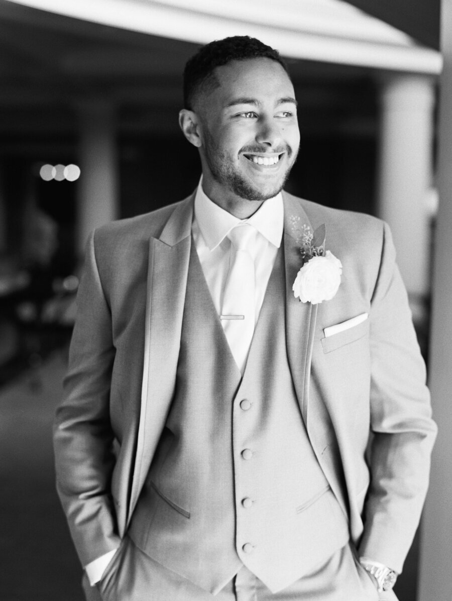 black and white photo of groom in gray suit on wedding day smiling out window