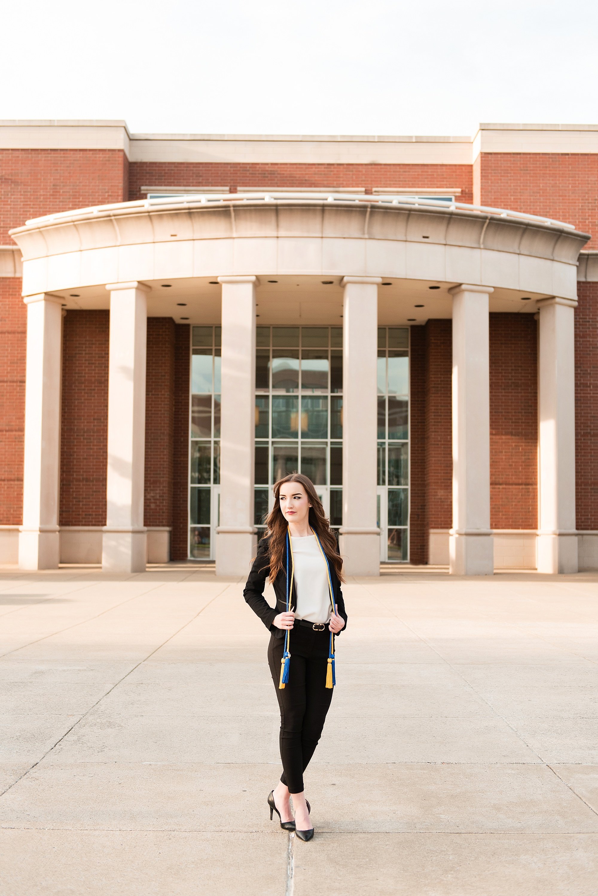 Senior standing in front of her college classes building on the MTSU campus wearing a fitted black suit and her graduation cords