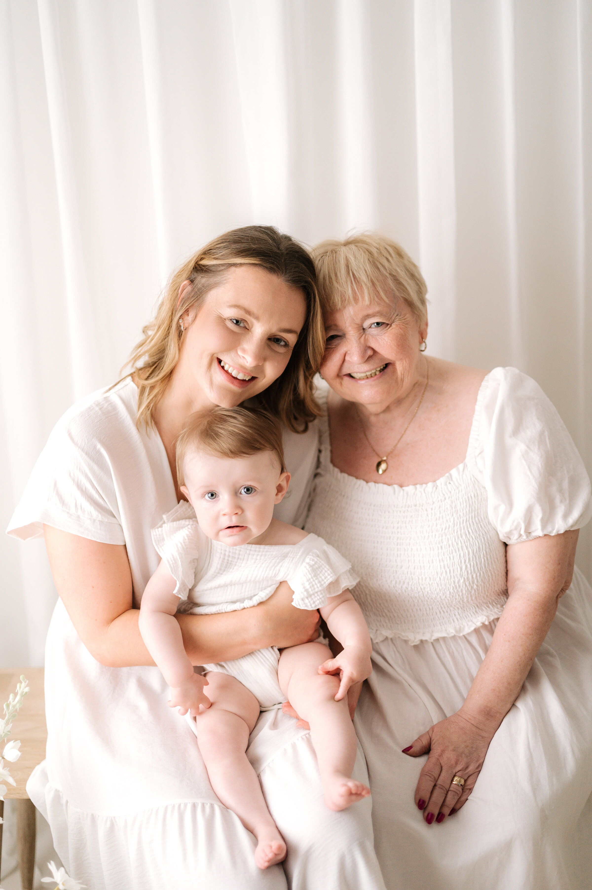 Mother holding her baby daughter with her grandmother smiling at a photoshoot in Horsham