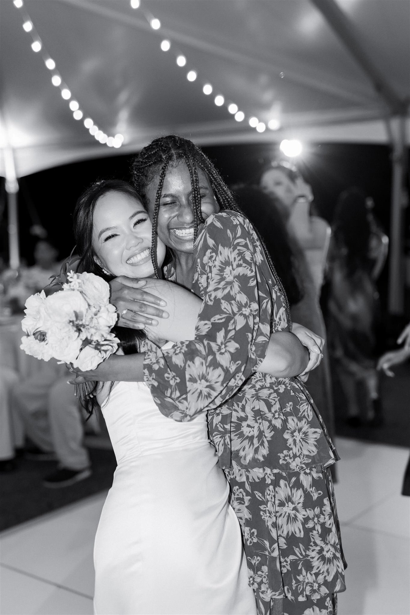 A newlywed hugging a wedding guests as they both smile brightly 