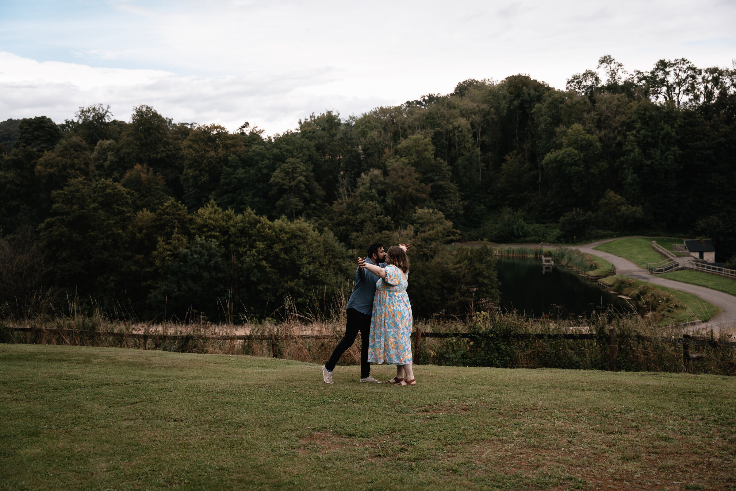 Couple dancing together on the grass with forest in background